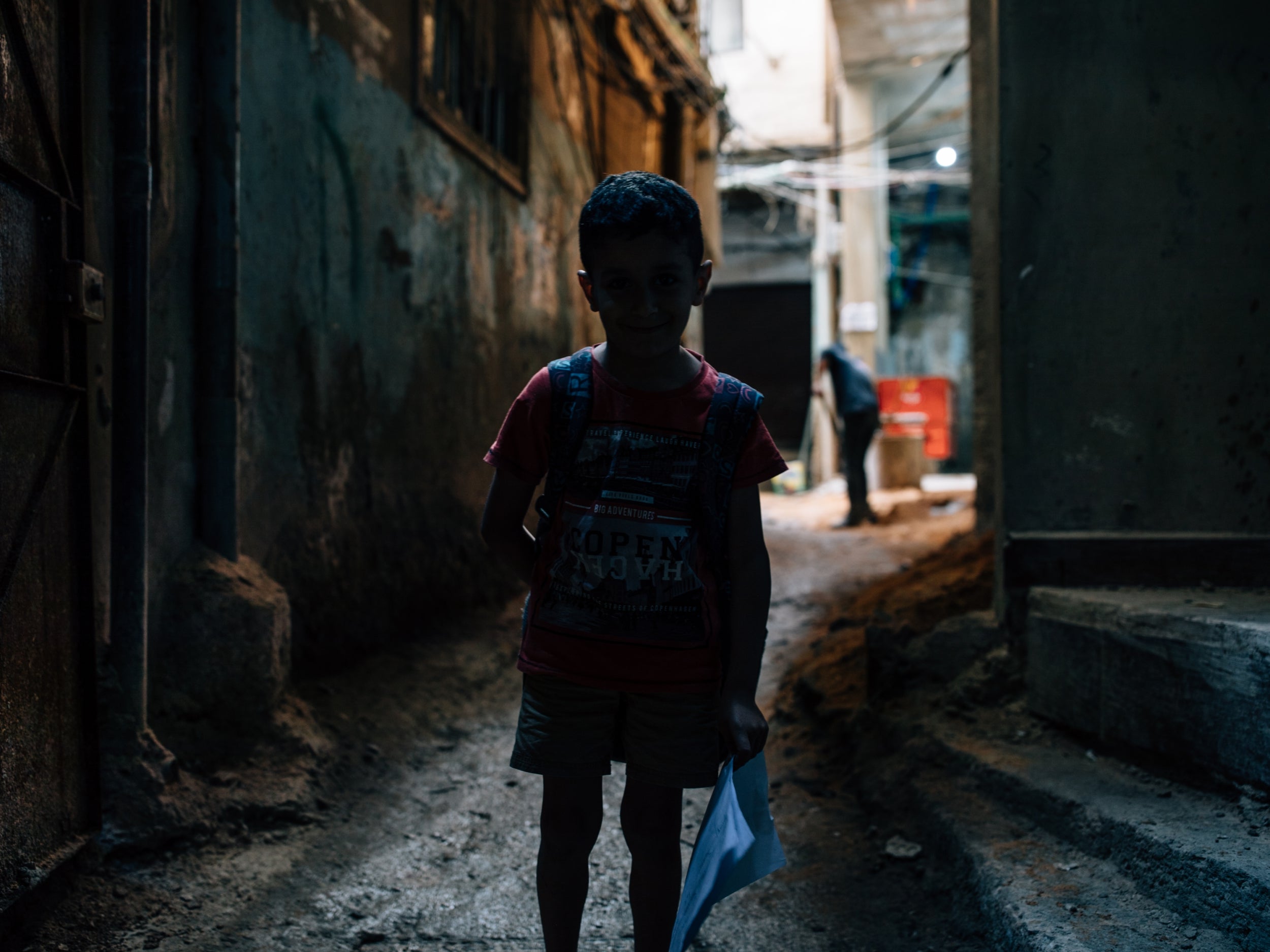 A young boy returning home from school down the dark alleyways of Bourj al-Barajneh camp