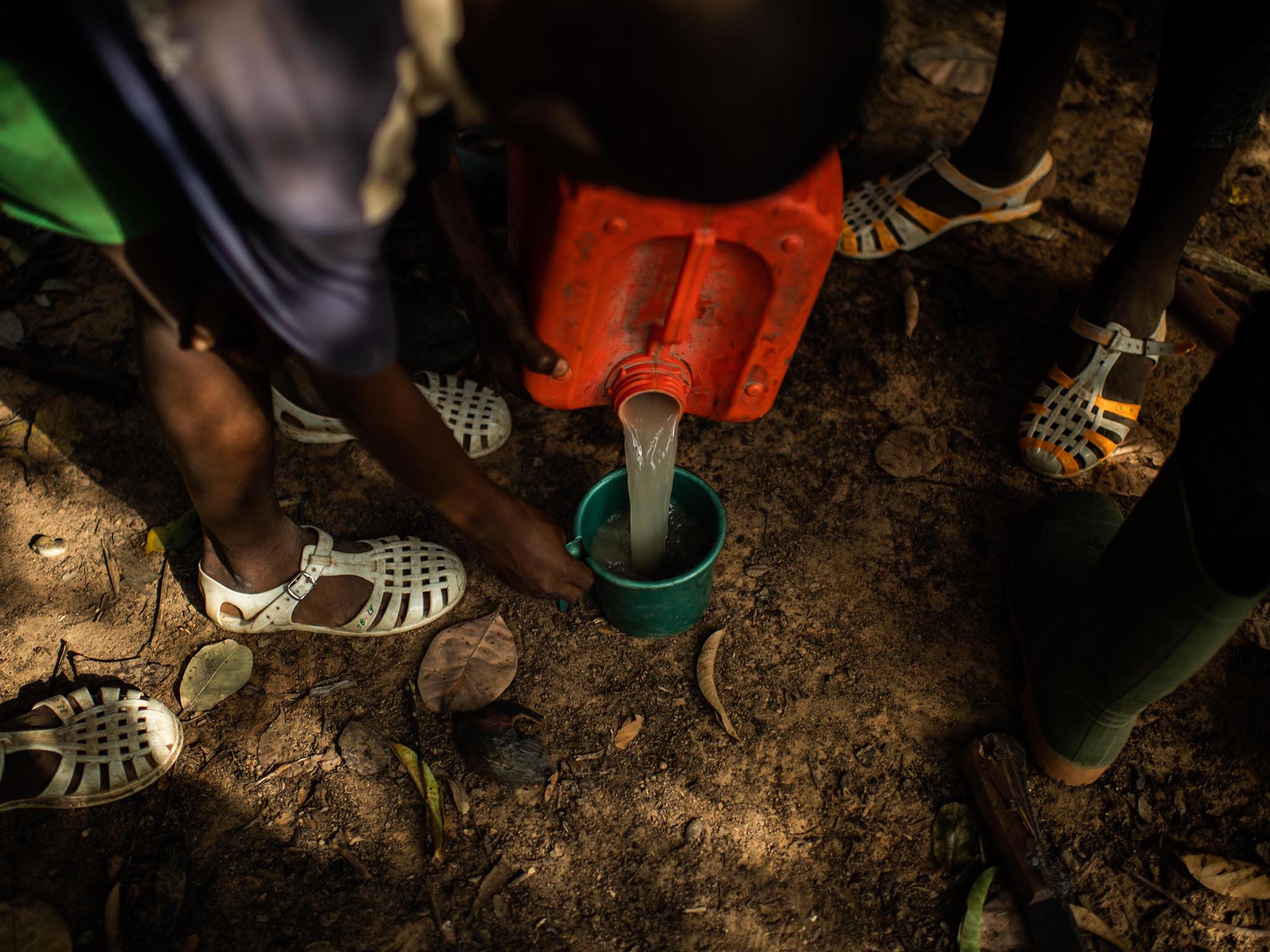 Children on a break from work at a cocoa farm share white-coloured water that was scooped into a bucket from a nearby pond