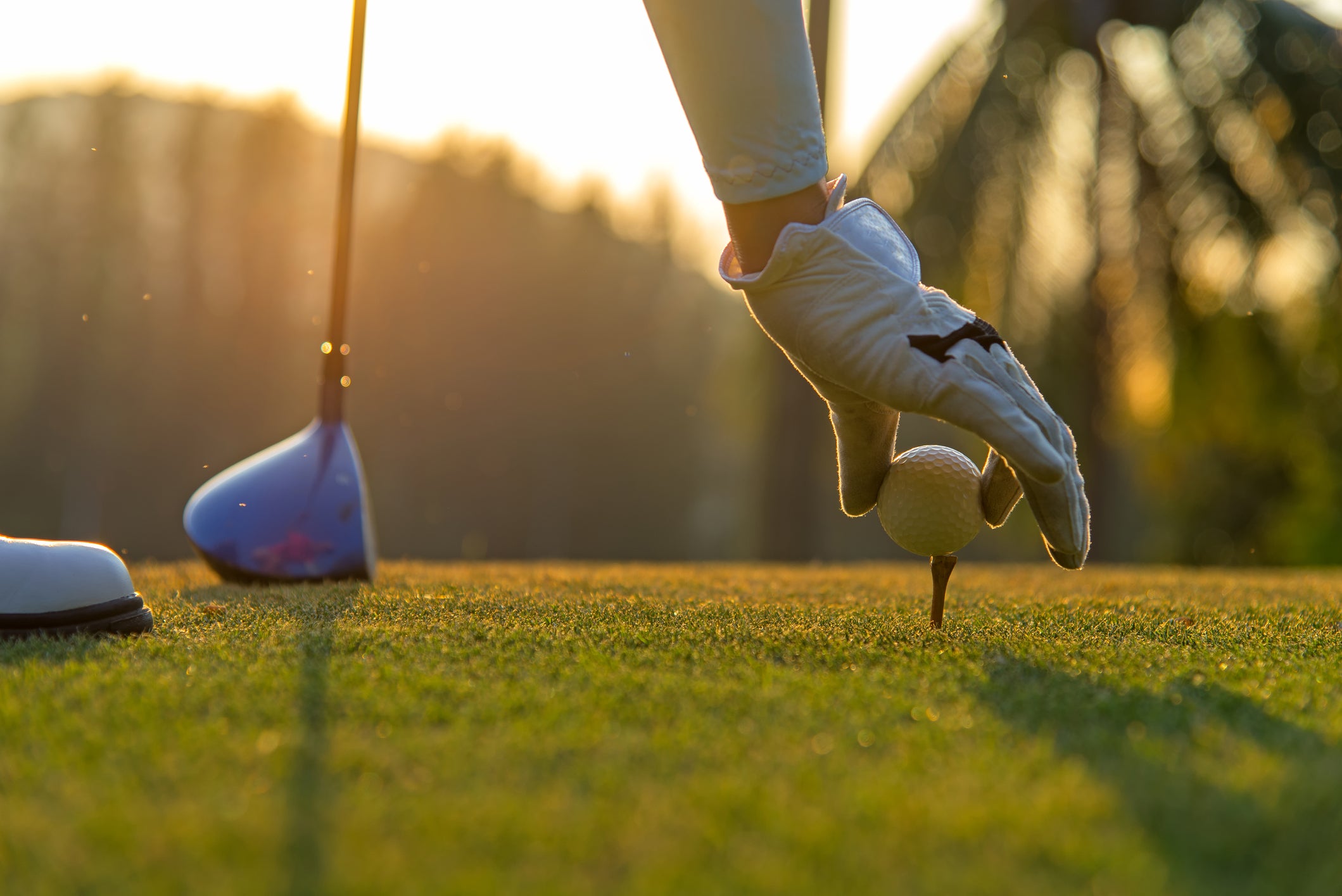 Woman putting golf ball on tee with club in golf course