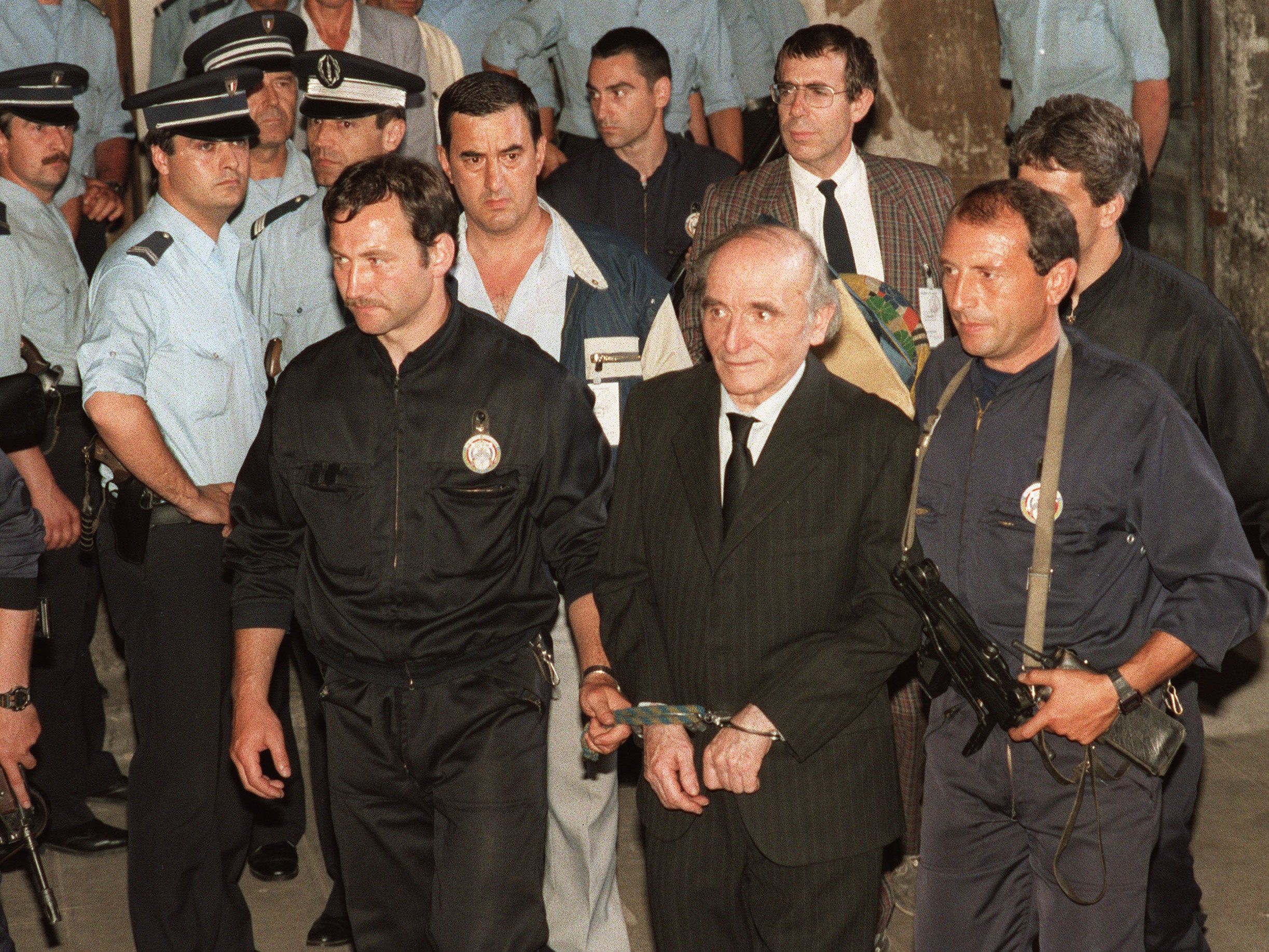 Handcuffed, Nazi war criminal Klaus Barbie is escorted out of Lyons courthouse after being sentenced to life behind bars
