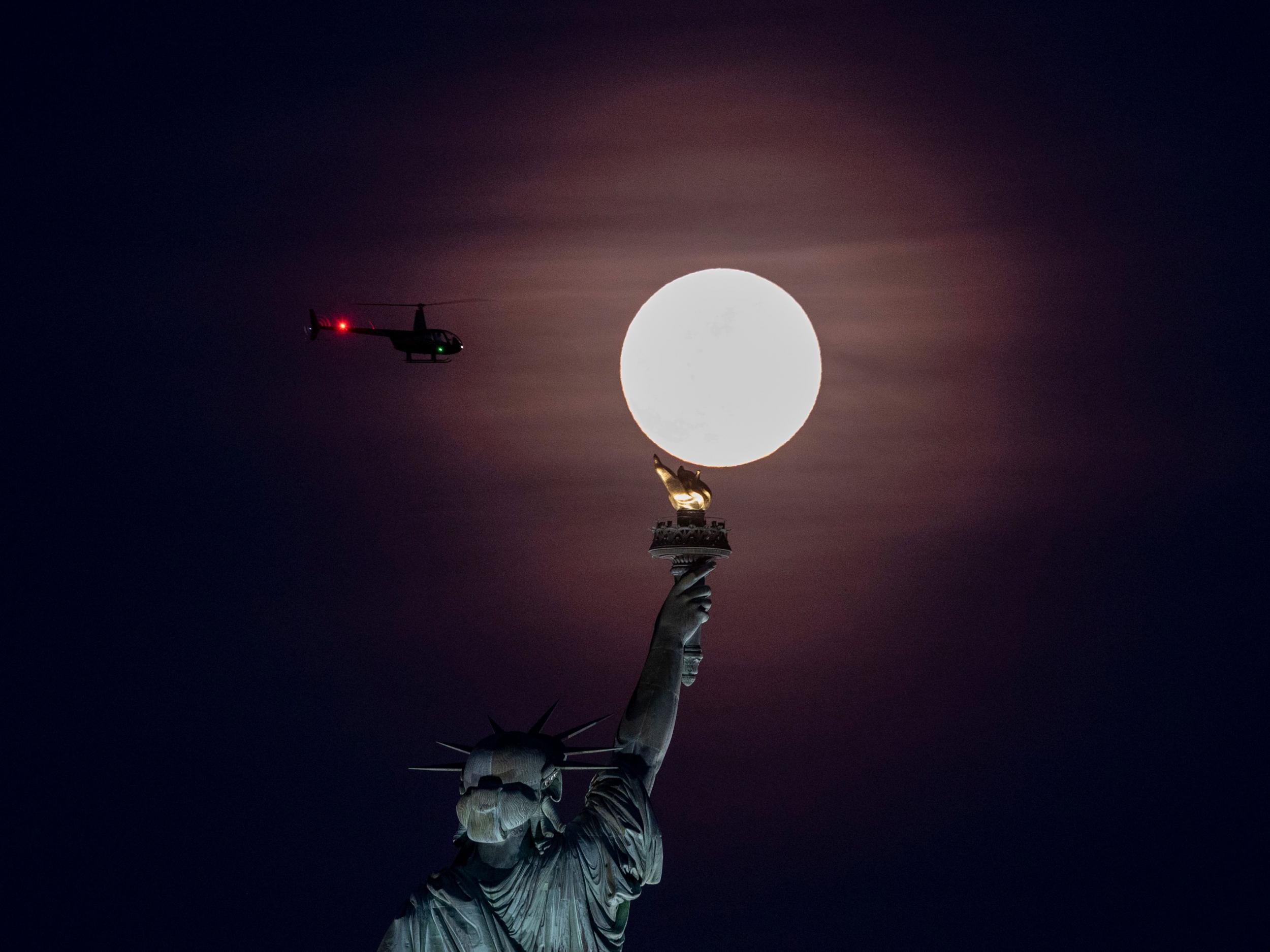 The full moon rises behind the Statue of Liberty in New York