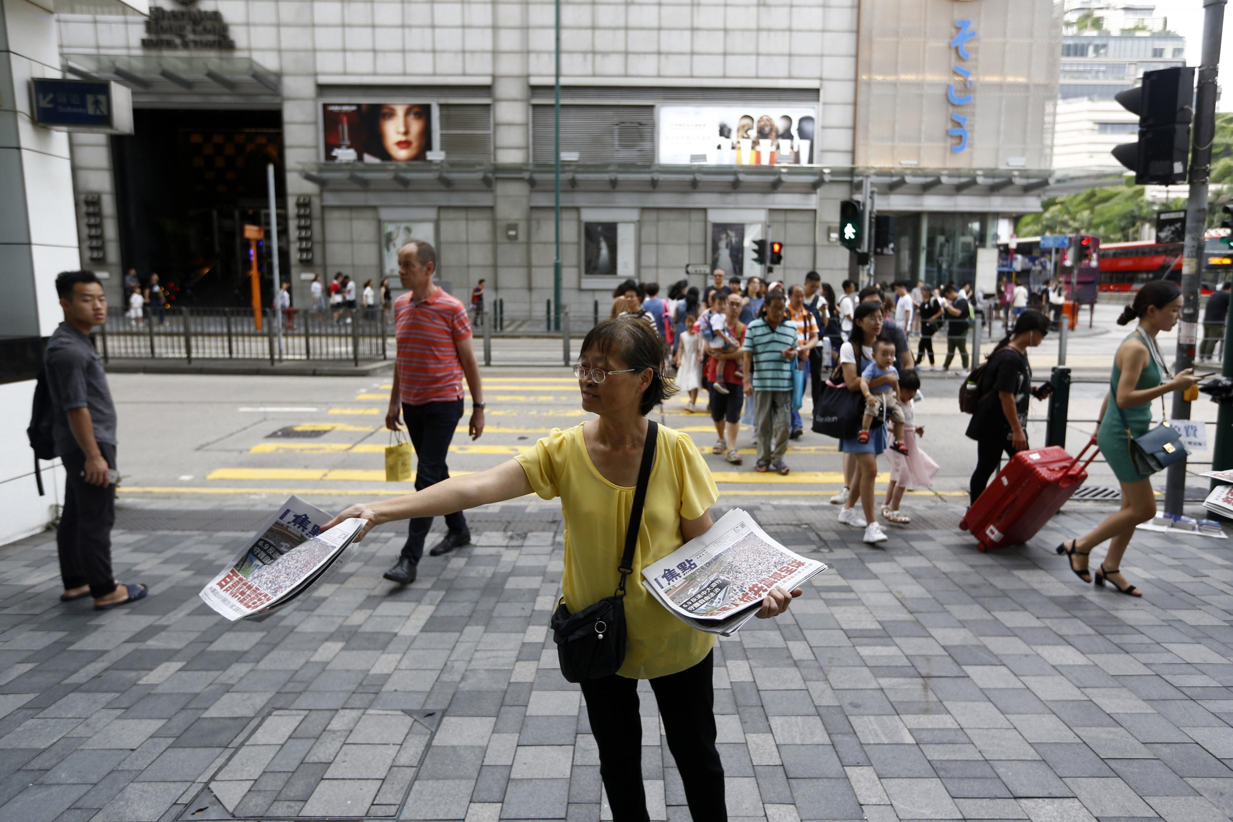 A woman distributes newspapers with the headlines “Millions against Communist China shock the world” in a shopping district popular with mainland Chinese tourists in Hong Kong