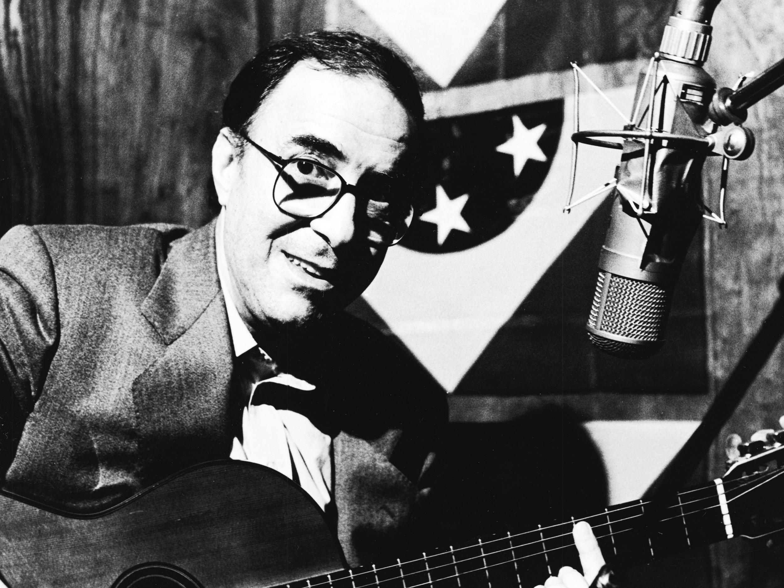 Gilberto strums his guitar in front of a microphone during a 1989 studio session