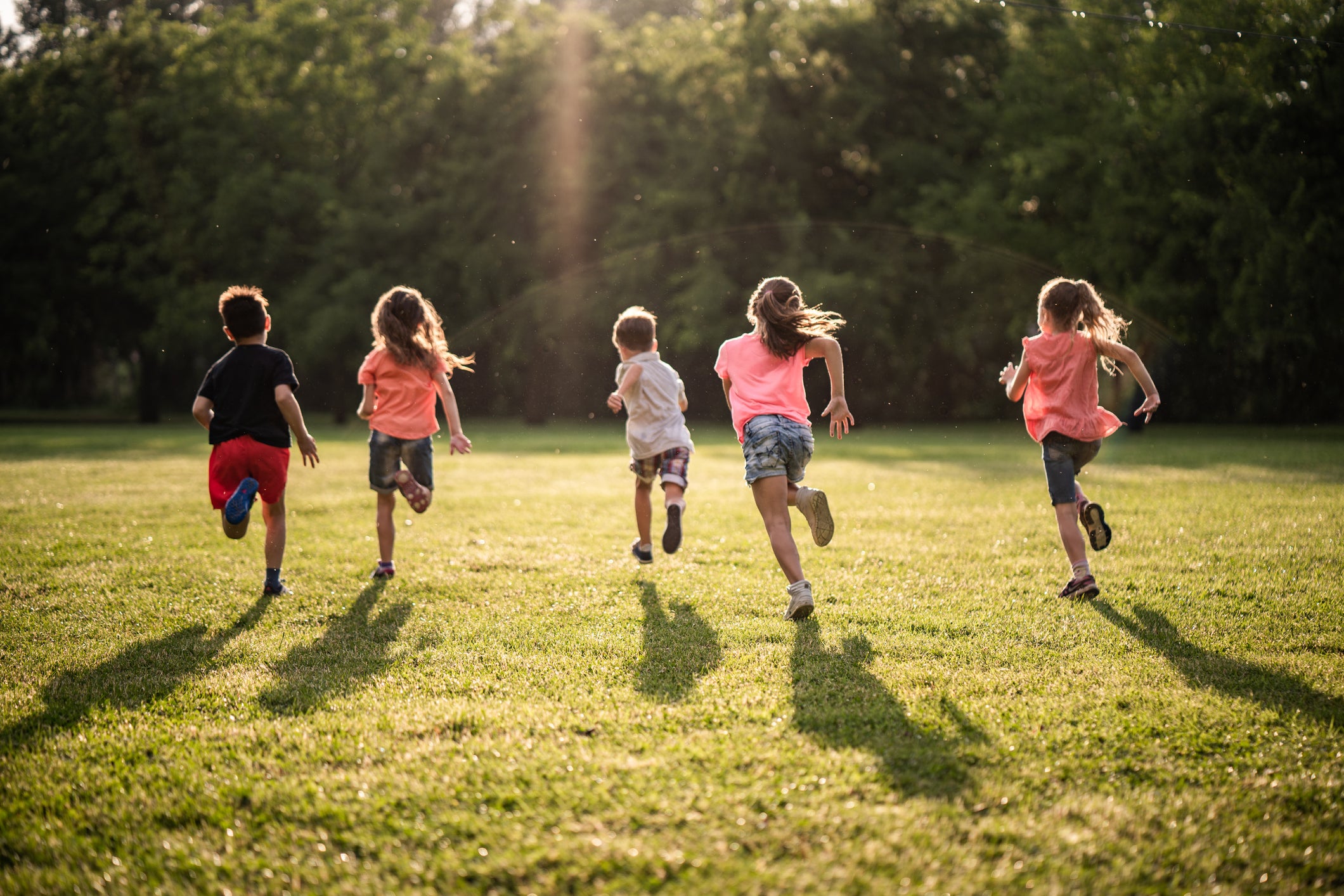 Back view children running together in public park at sunset