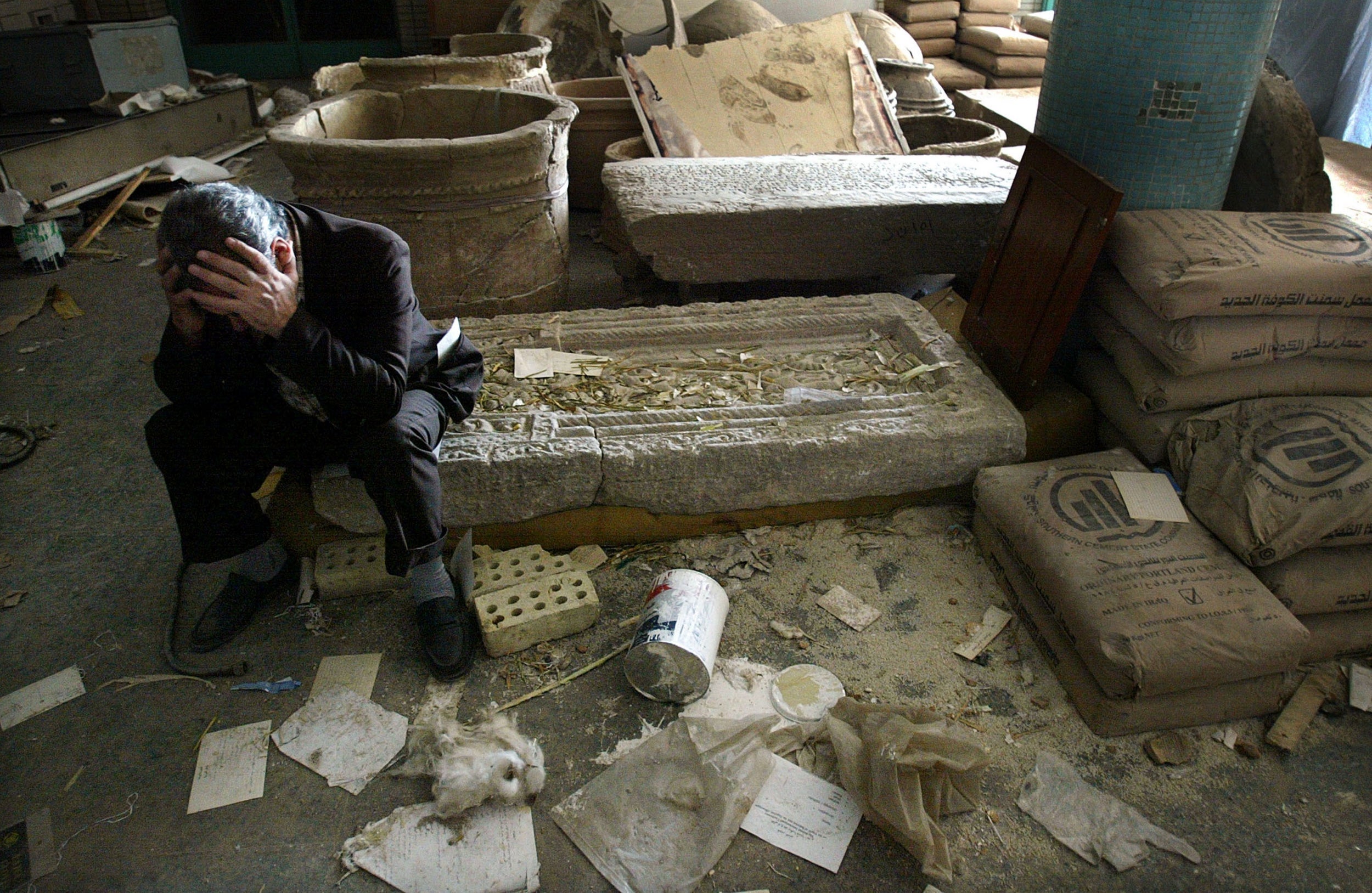 The museum’s deputy director, Mushin Hasan, holds his head in his hands as he sits on destroyed artefacts in April 2003 in Baghdad (Getty)