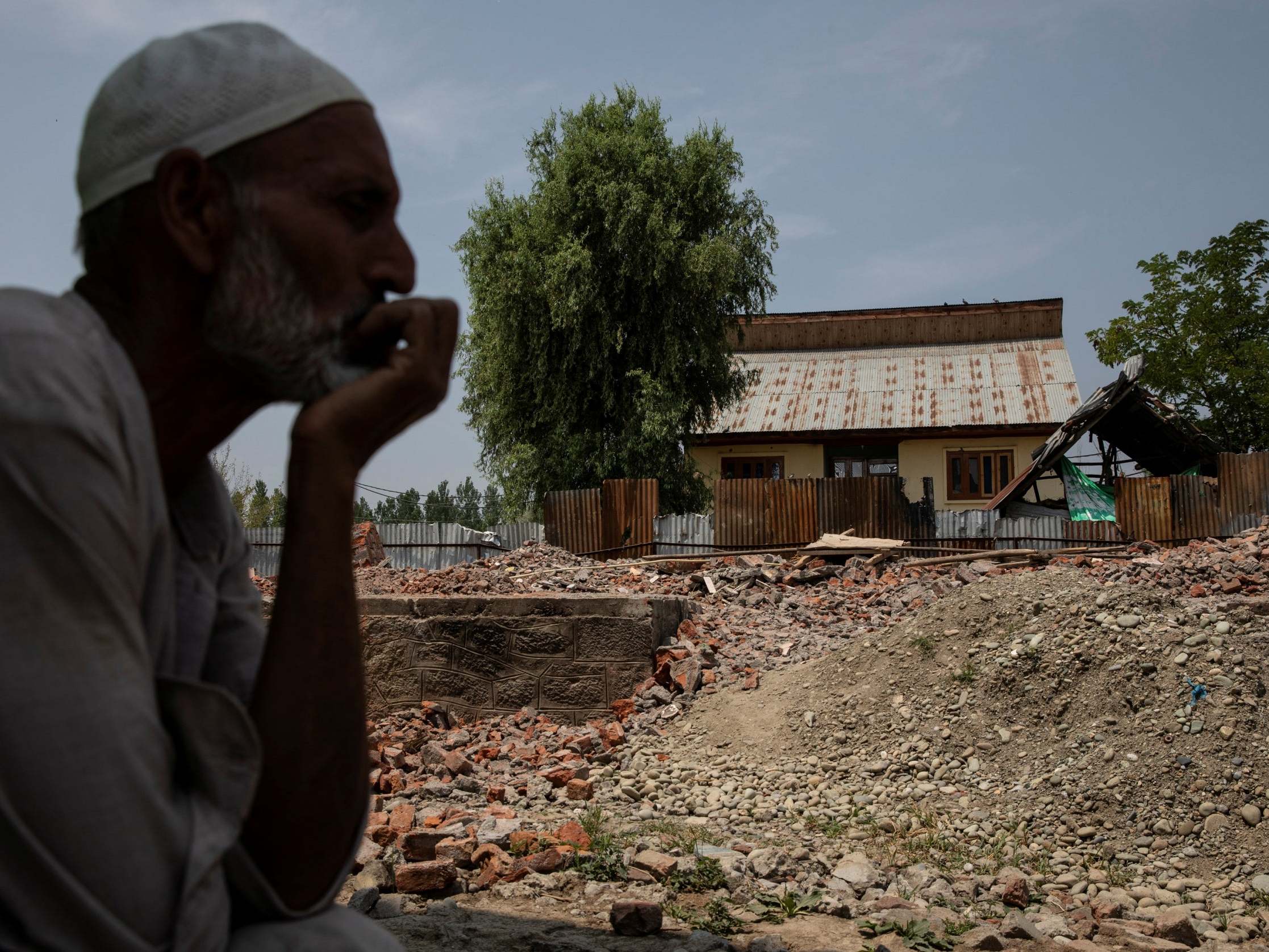 Abdul Hamid Mir, uncle of Atif Mir, 12, who was taken hostage by militants and later killed in crossfire with Indian troops, sits next to his destroyed house