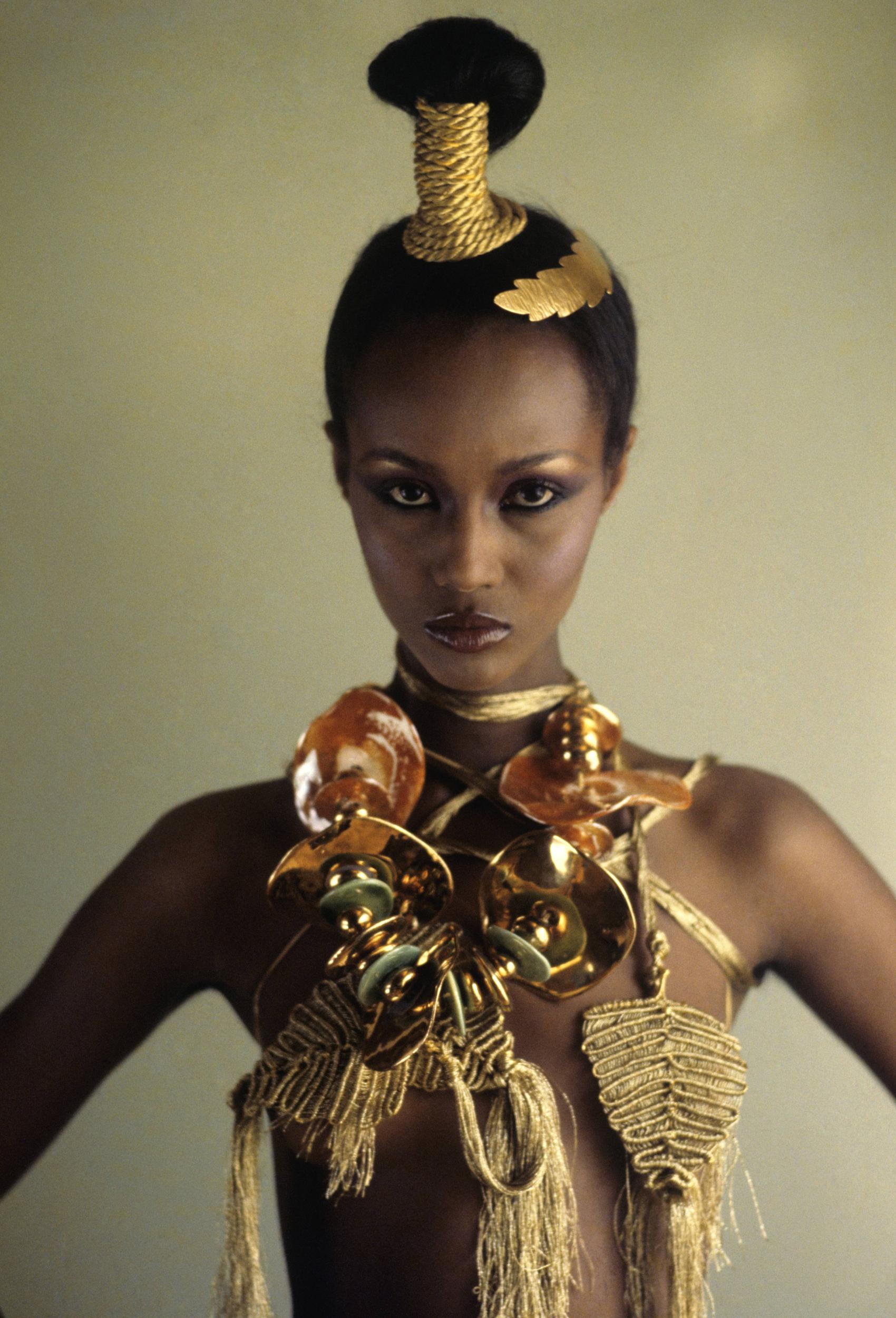 Close up of model, Iman, wearing Mary McFadden’s head and body wrap of gold macrame and non-jewel jewels.