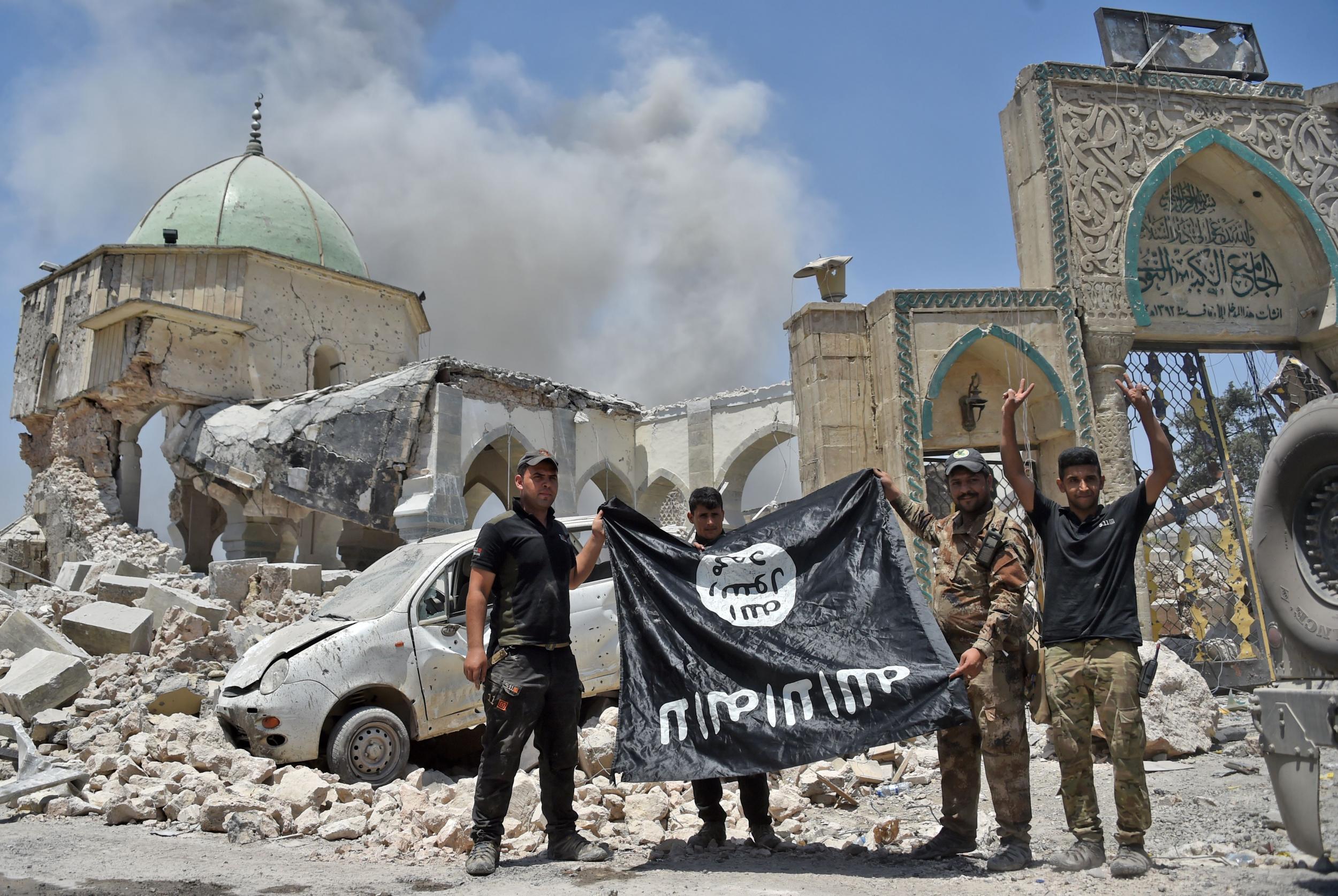 As a victory gesture, Iraqis hold an upside-down black flag of Isis outside the destroyed Al-Nuri Mosque in the Old City of Mosul (AFP/Getty)