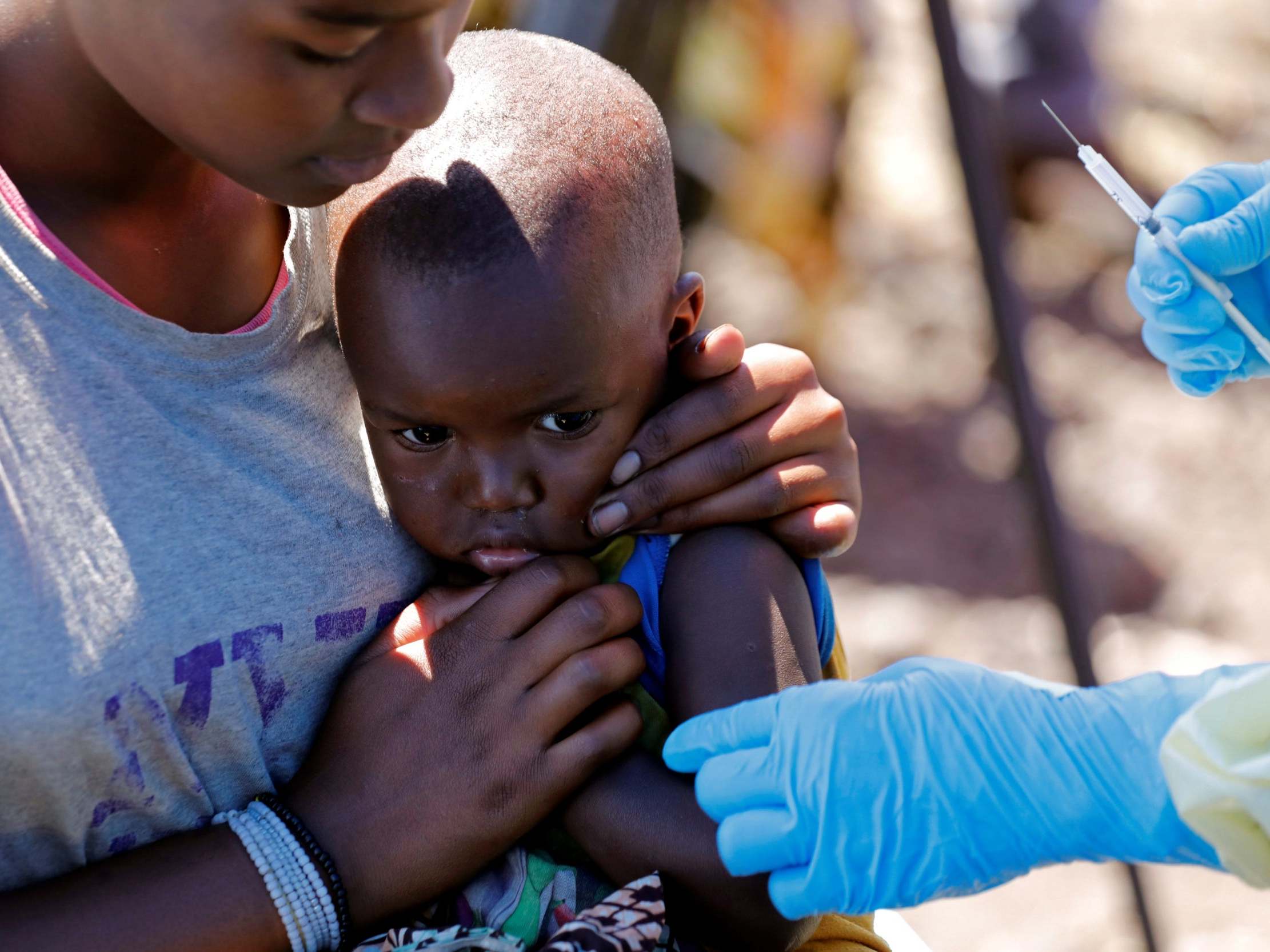 A mother caresses her baby as a medical worker administers the Ebola vaccine