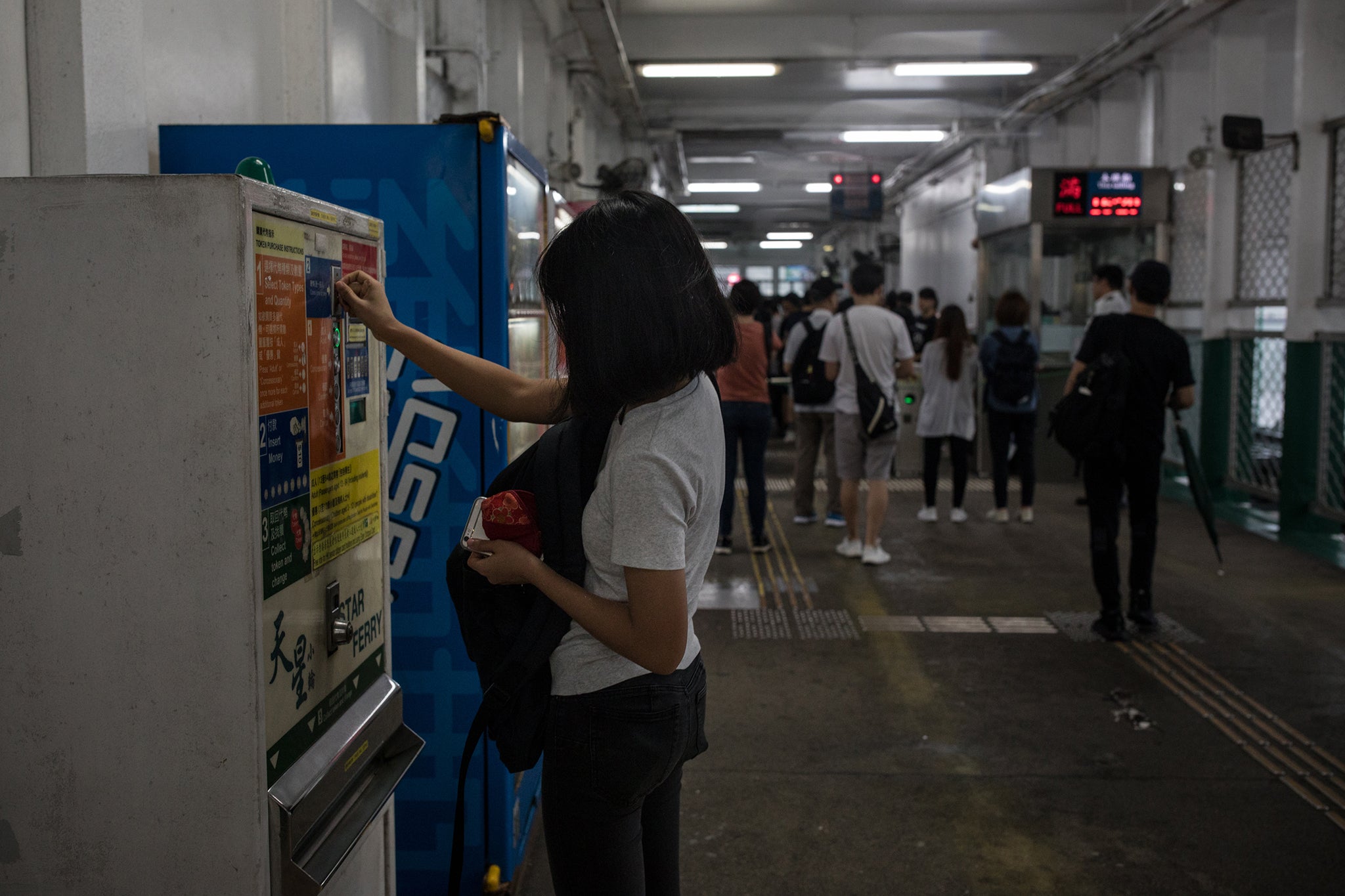 Gigi buys a token to take the ferry from Tsim Sha Tsui. She has opted not to use the prepaid transportation card to avoid being tracked