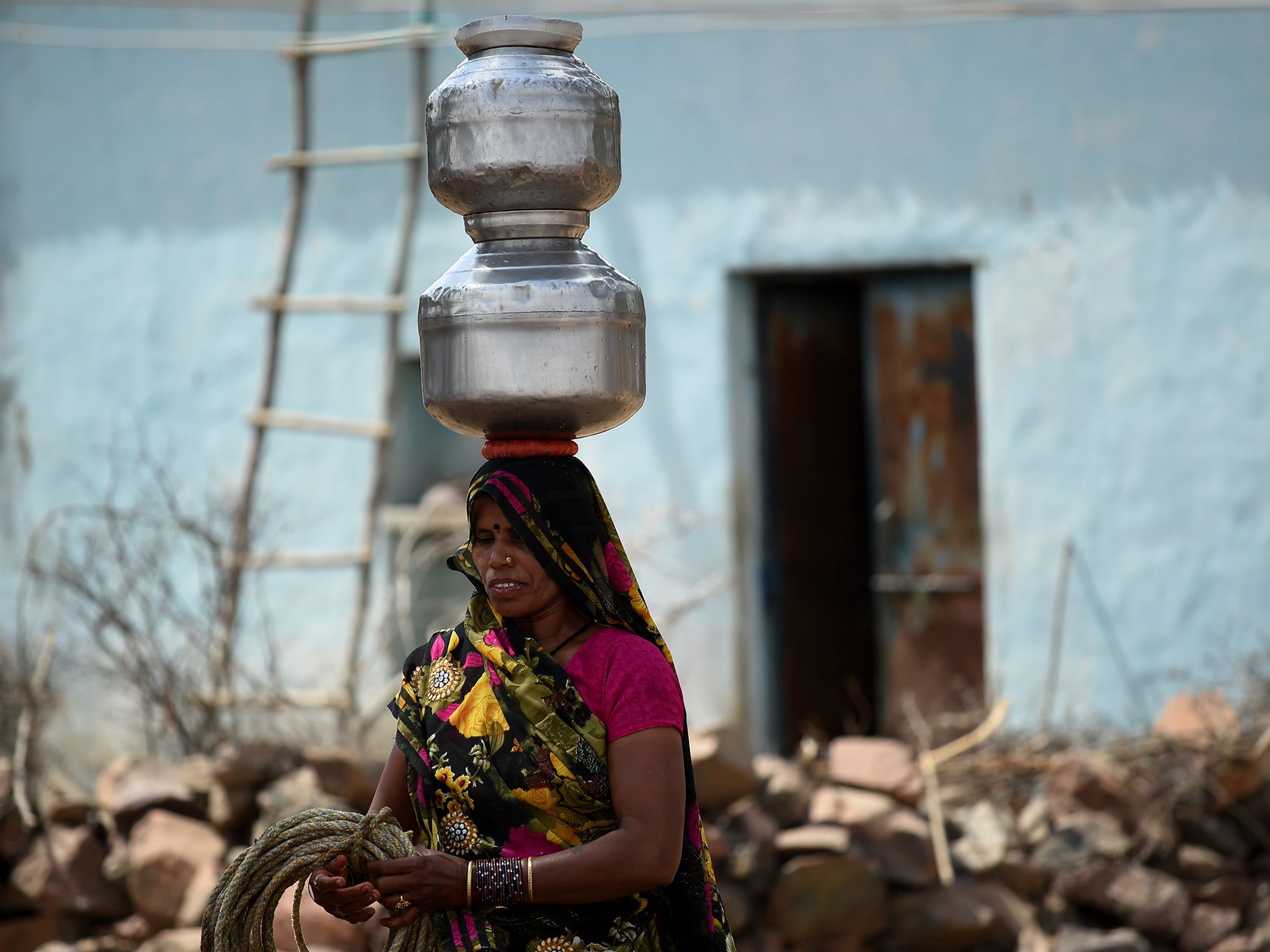 A woman carries pots of water after filling them from a well in Dargai Khurd village