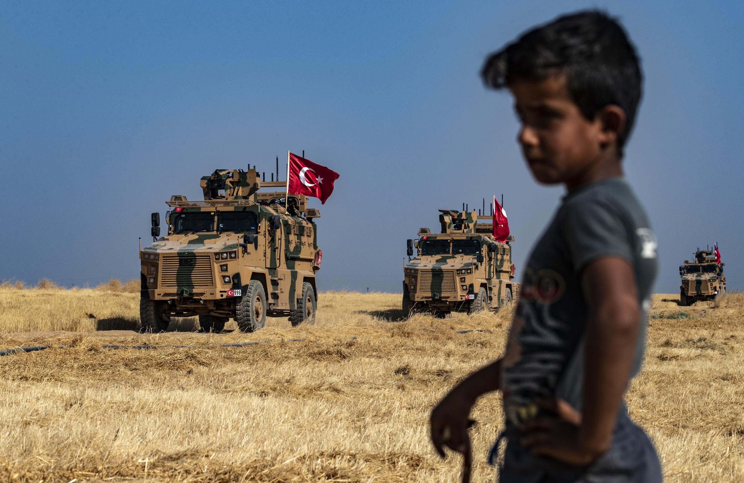 A Syrian boy watches as Turkish military vehicles, part of a US military convoy, take part in a joint patrol in the Syrian village on the outskirts of Tal Abyad town