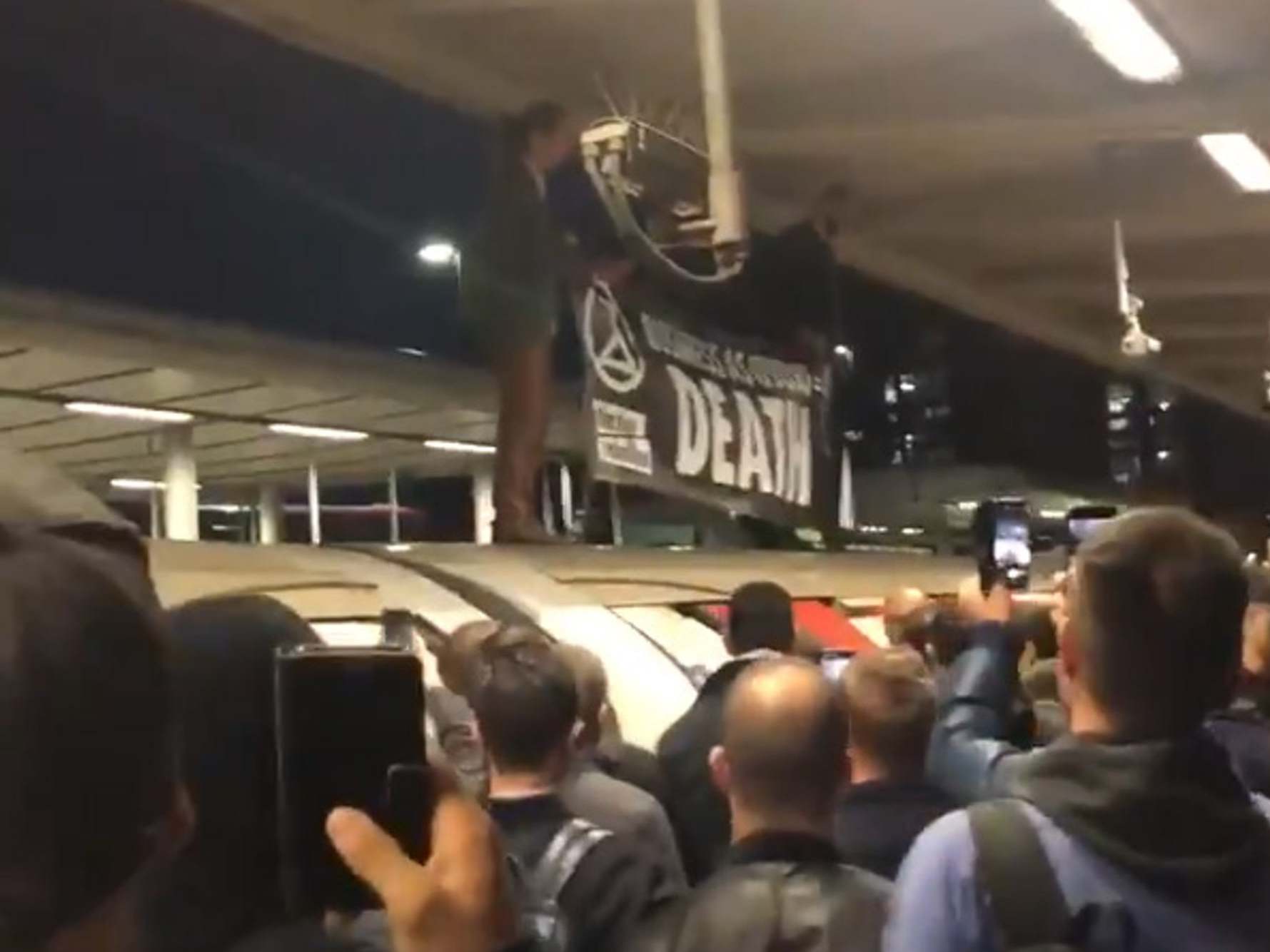 Extinction Rebellion protesters on the roof of an Underground train surrounded by angry commuters at Canning Town station in east London (@CharWilkoo/PA)