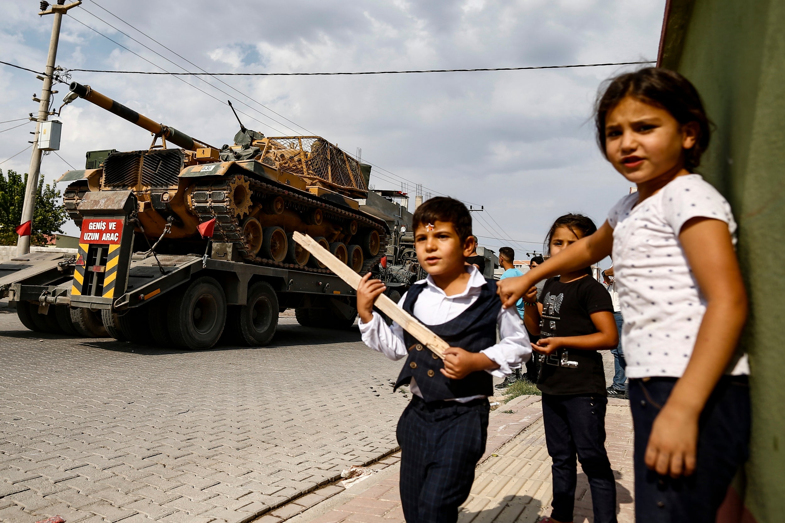 Children watch as army tanks are transported on trucks in the outskirts of border town Akcakale on Thursday