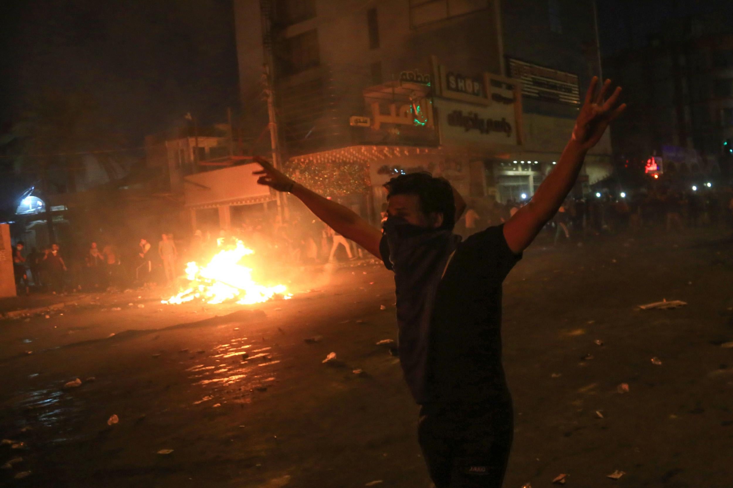 A protester gestures as burning tyres light up the night skies during anti-government protests in the Shia shrine city of Karbala