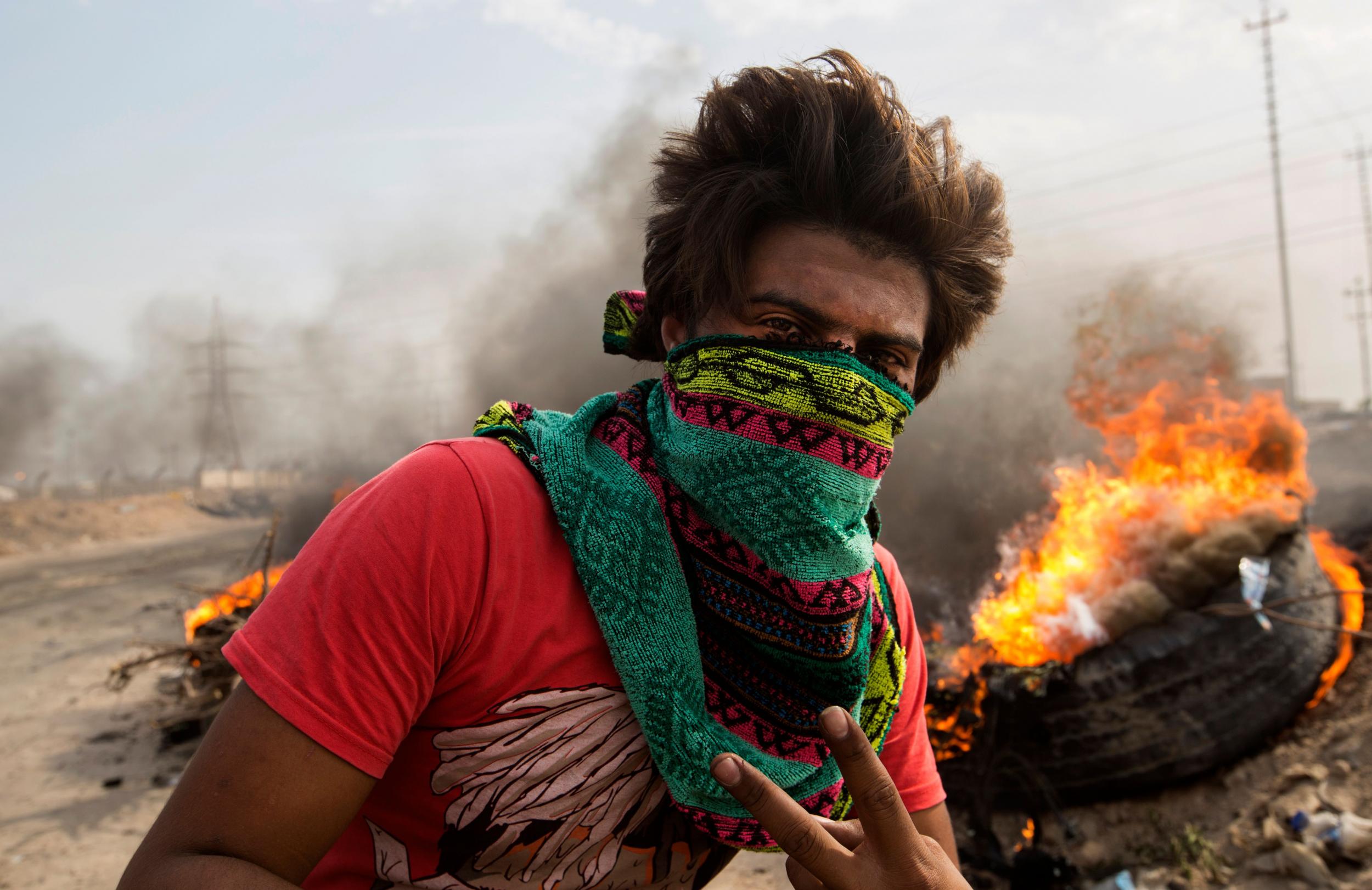 An Iraqi protester walks past burning tires as others block the road to Umm Qasr port during ongoing anti-government demonstrations in southern Iraq