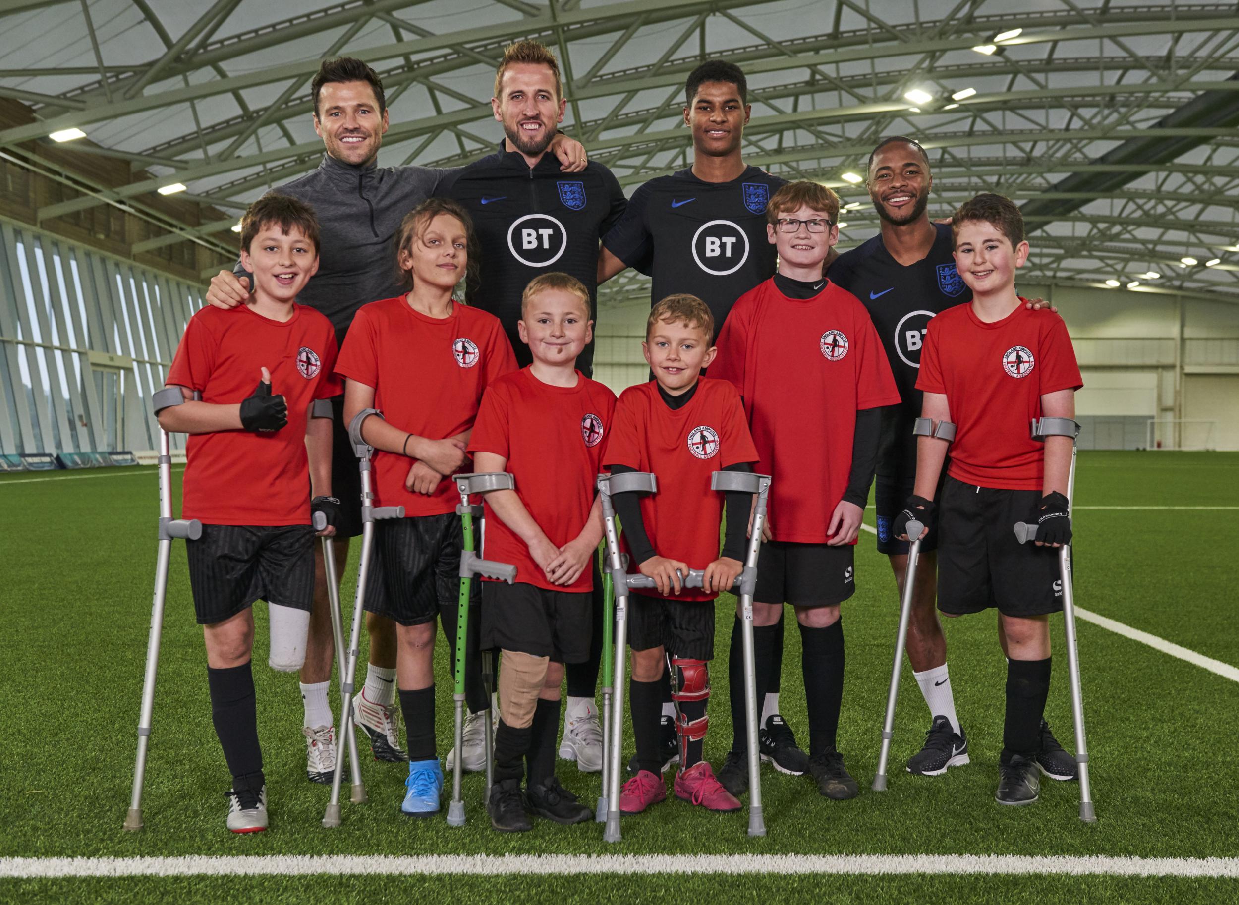 Members of the national football team pose with children from the England Amputee Football Association