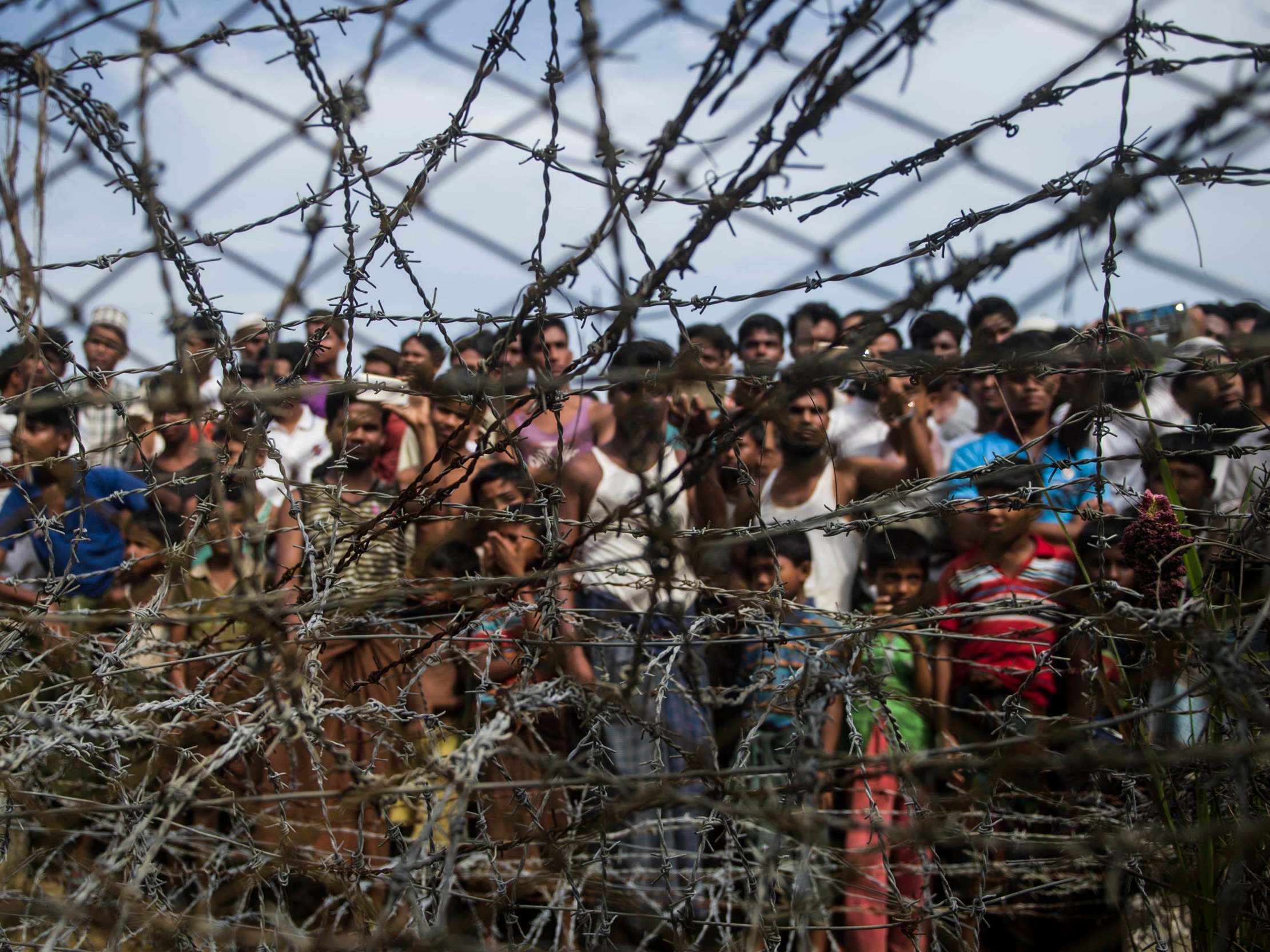 Rohingya refugees gather behind a barbed-wire fence in a temporary settlement set up in a 'no man's land' border zone between Myanmar and Bangladesh