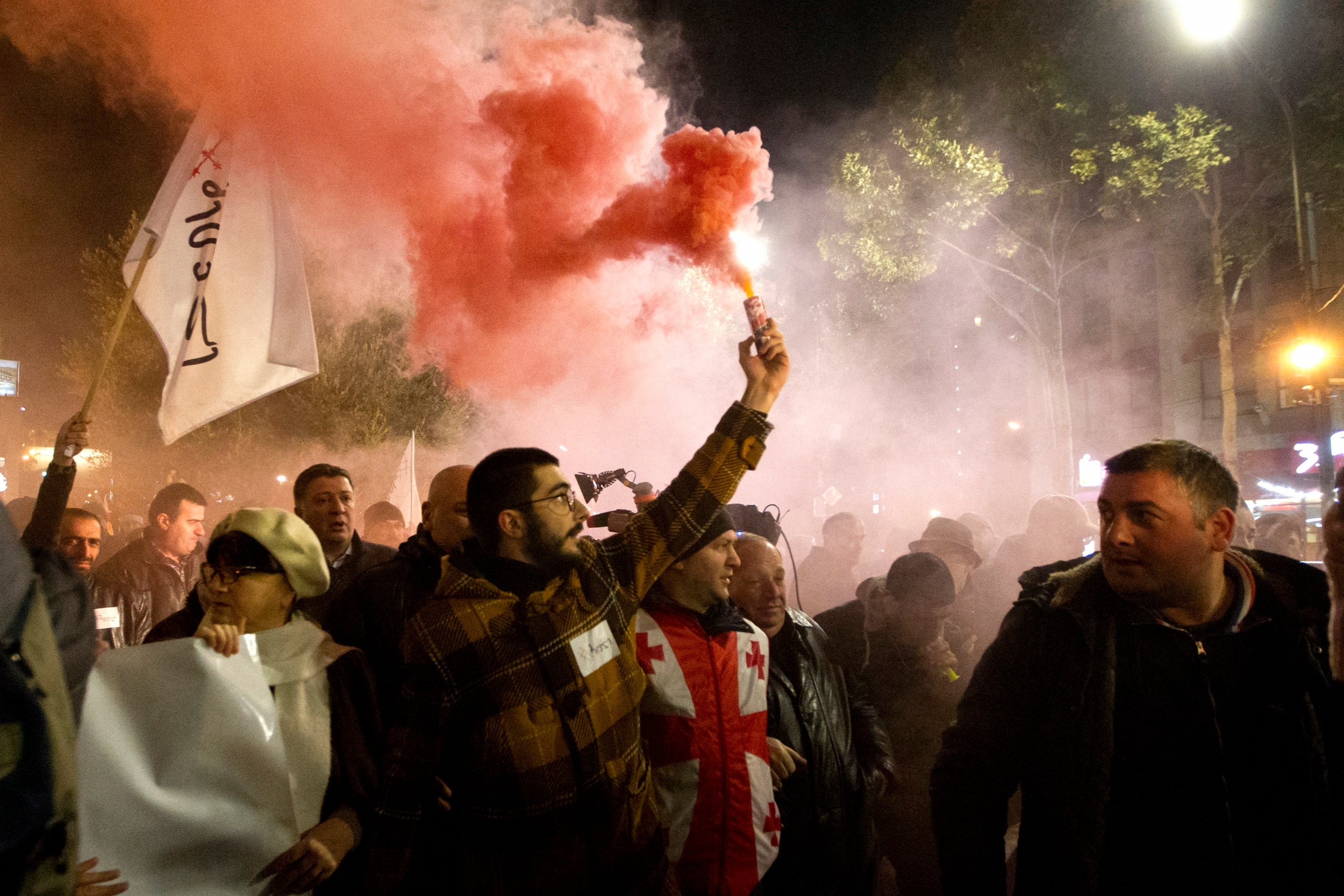 Protesters light flares as they gather at the Georgian parliament building in Tbilisi, Georgia