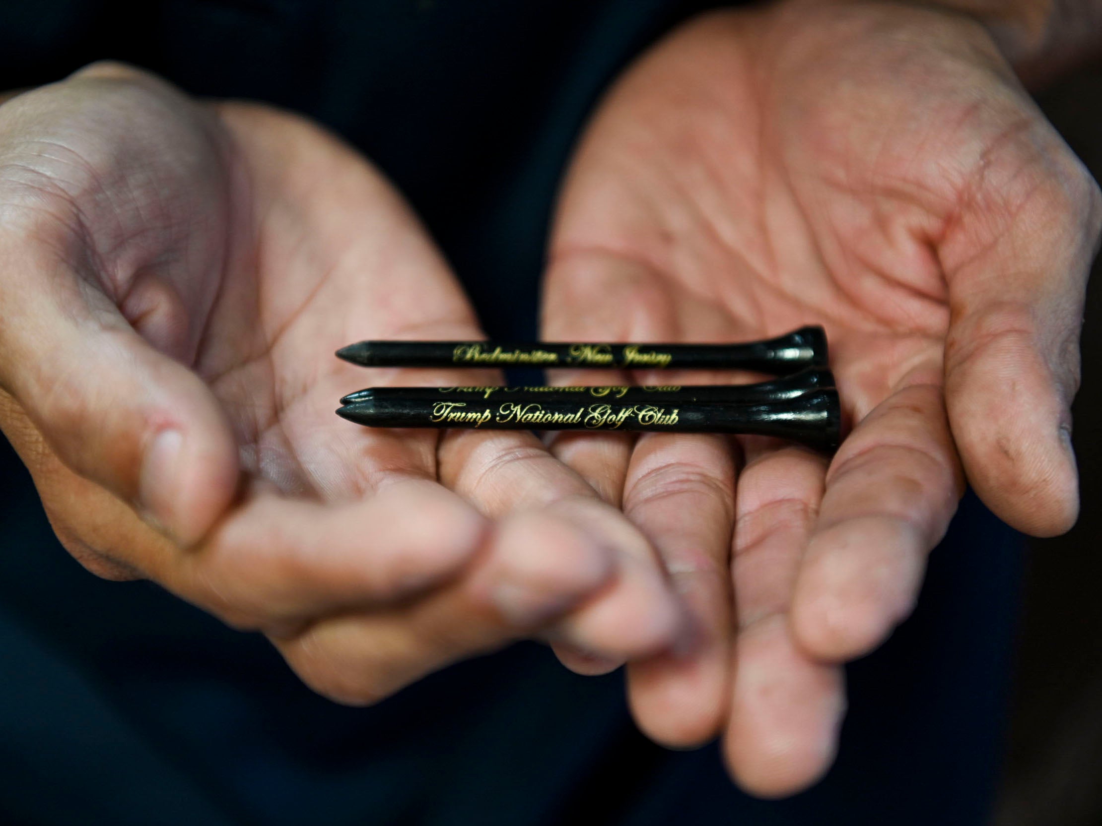 A former undocumented worker holds golf tees and wears a shirt from Trump National Golf Club Bedminster