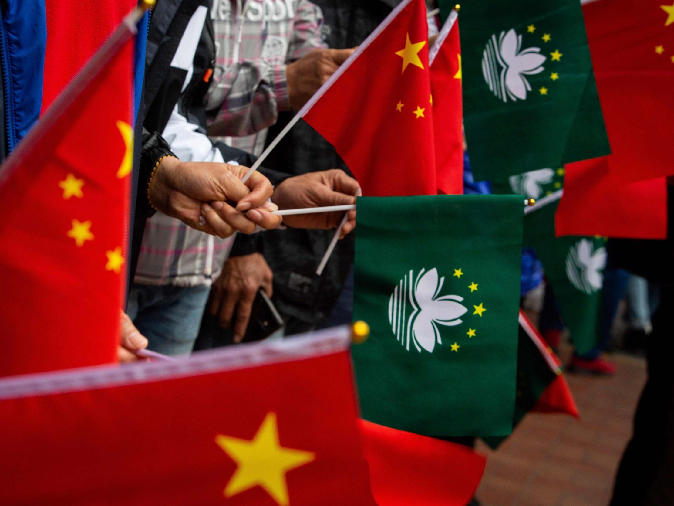 People hold China and Macau flags before the motorcade of President Xi passes (AFP/Getty)