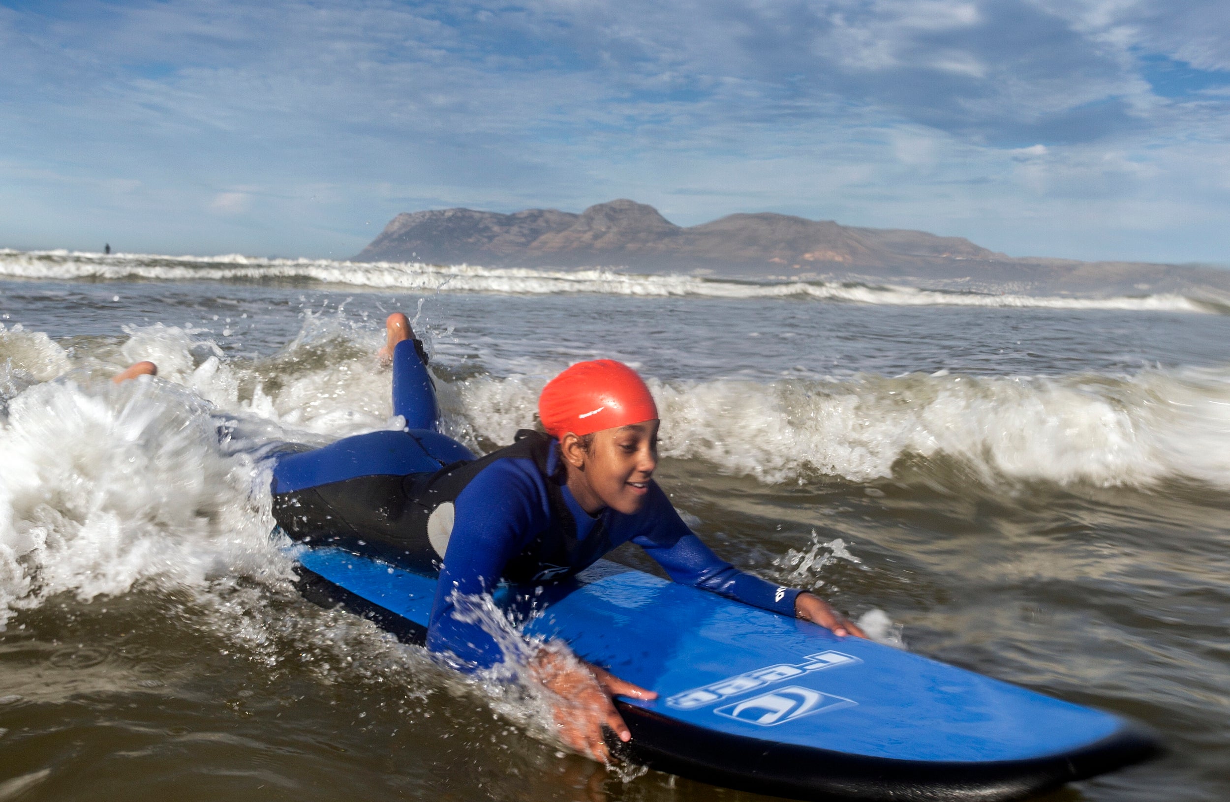 A child living on the Autism spectrum rides a wave in the ocean at Muizenberg beach, Cape Town, South Africa. Waves for Change is an organisation that uses surfing as a form of therapy to help children who are on the autism spectrum