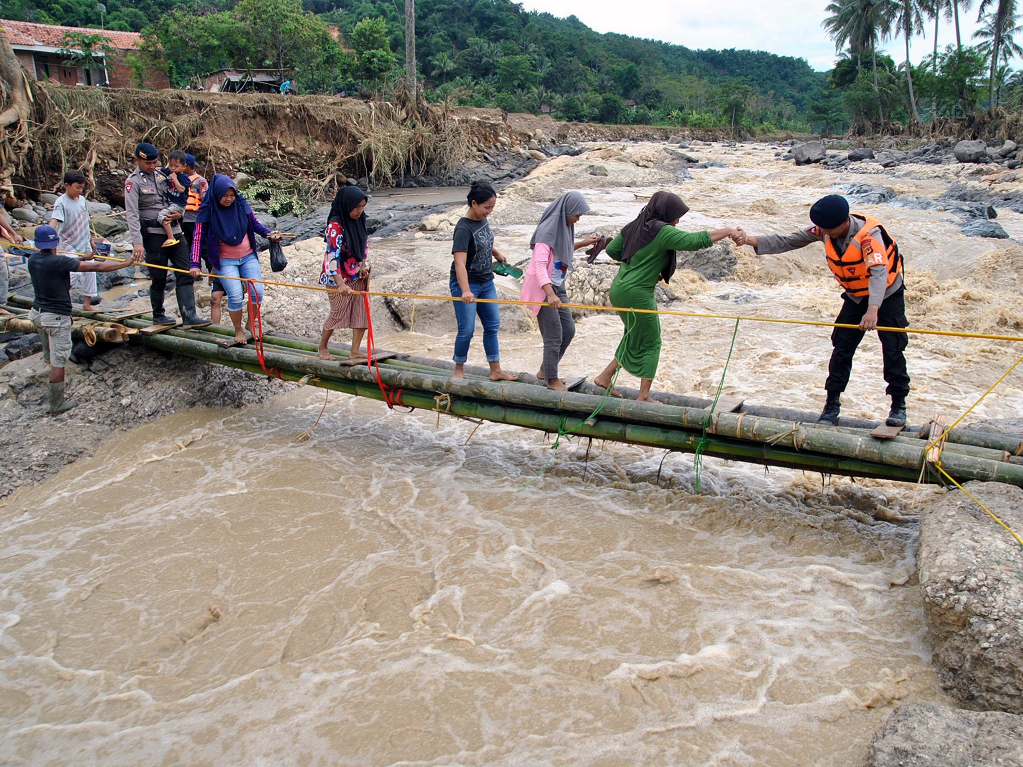 Police officers help people cross an emergency bridge over the Cidurian river