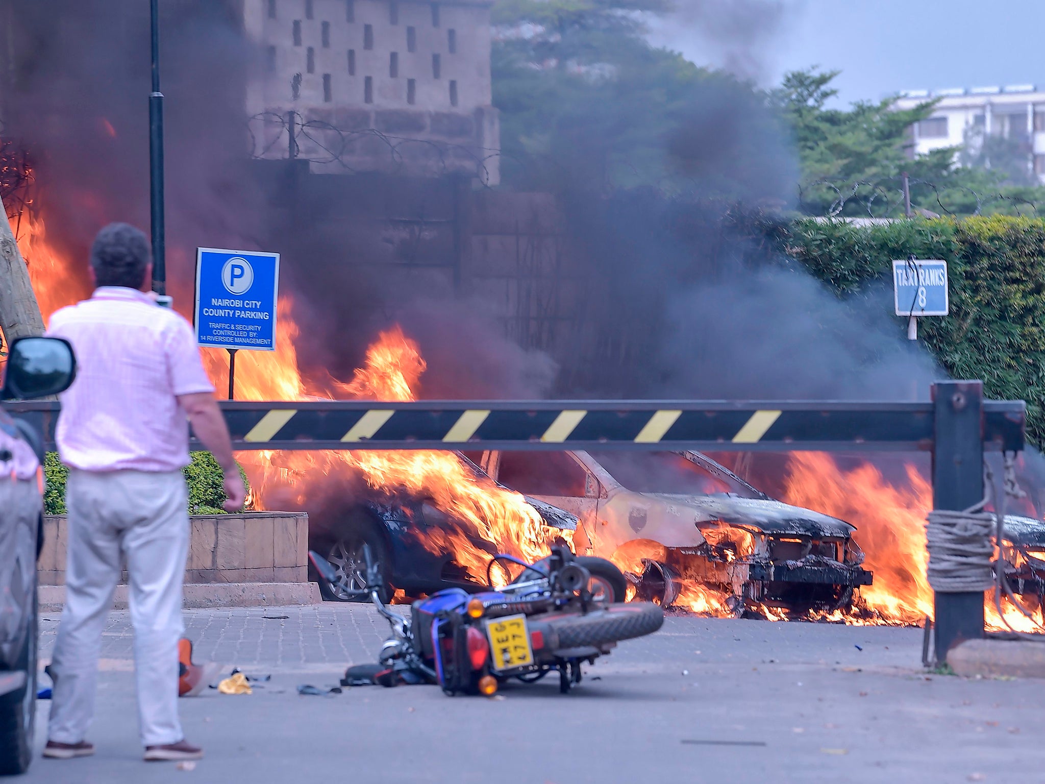 Two men stand next to burning cars at the scene of an explosion at a hotel complex in Nairobi