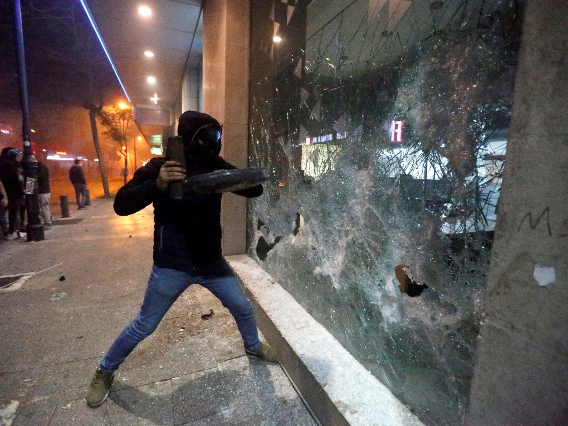 A protester smashes the window of a bank as demonstrations against the government continue in Beirut