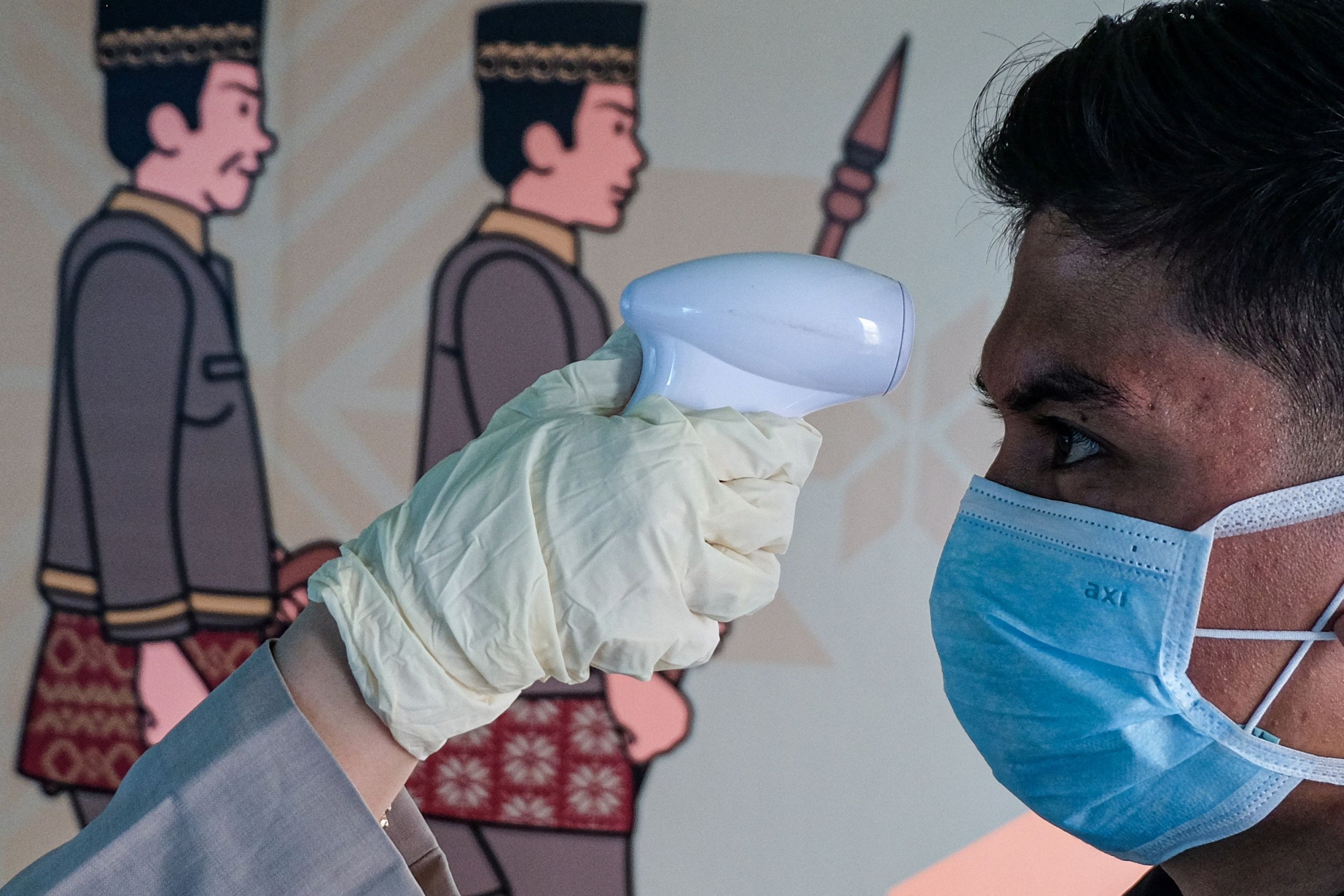 A person checks the temperature of a passenger wearing a facemask as he arrives at the Sultan Mahmud Badaruddin II International airport in Palembang