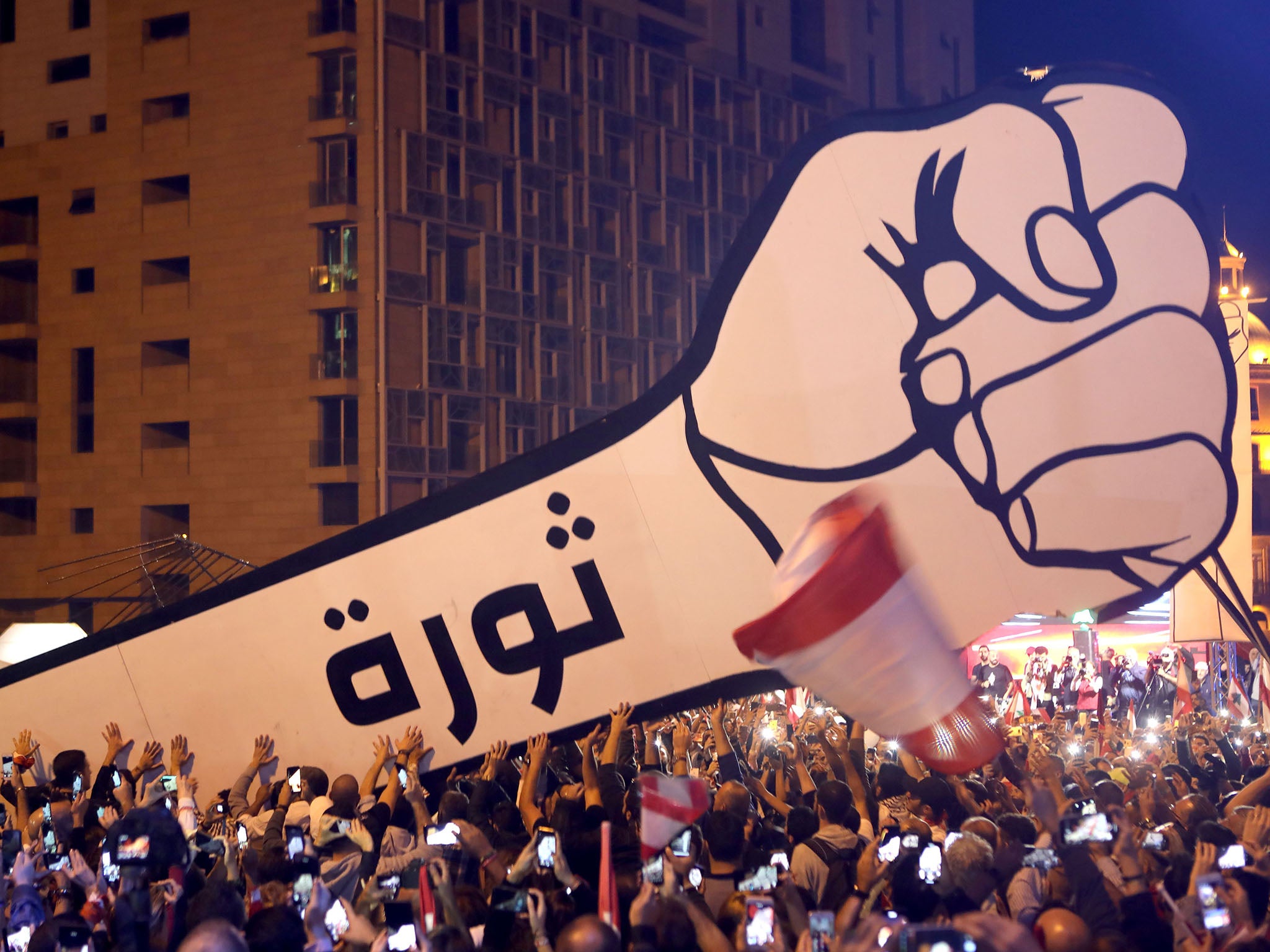 Lebanese protesters raise a giant fist that bears the Arabic word revolution