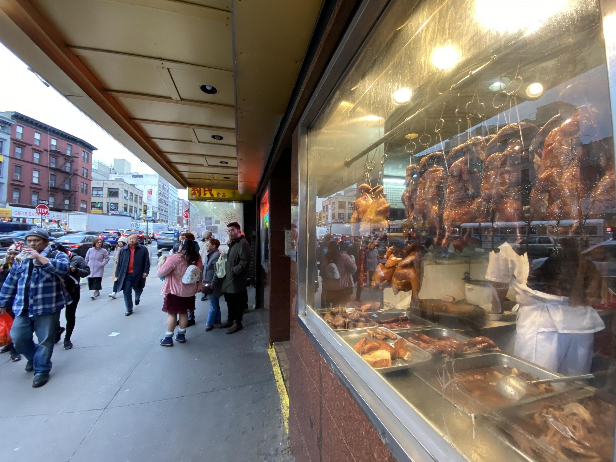 Pedestrians walk by Peking ducks in a Chinatown restaurant's window