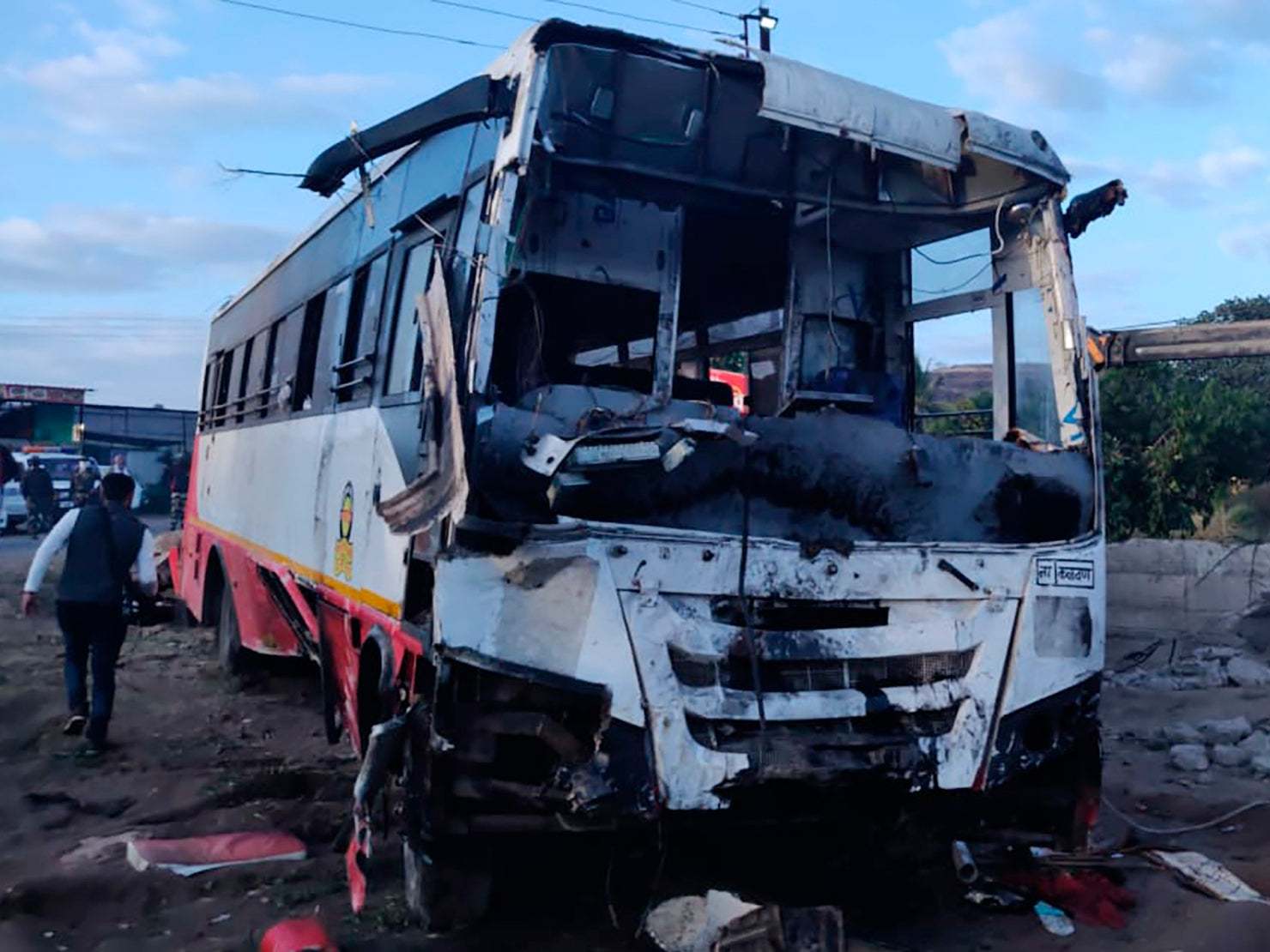 A man walks past the wrangled remains of a bus after an accident in Nashik, India