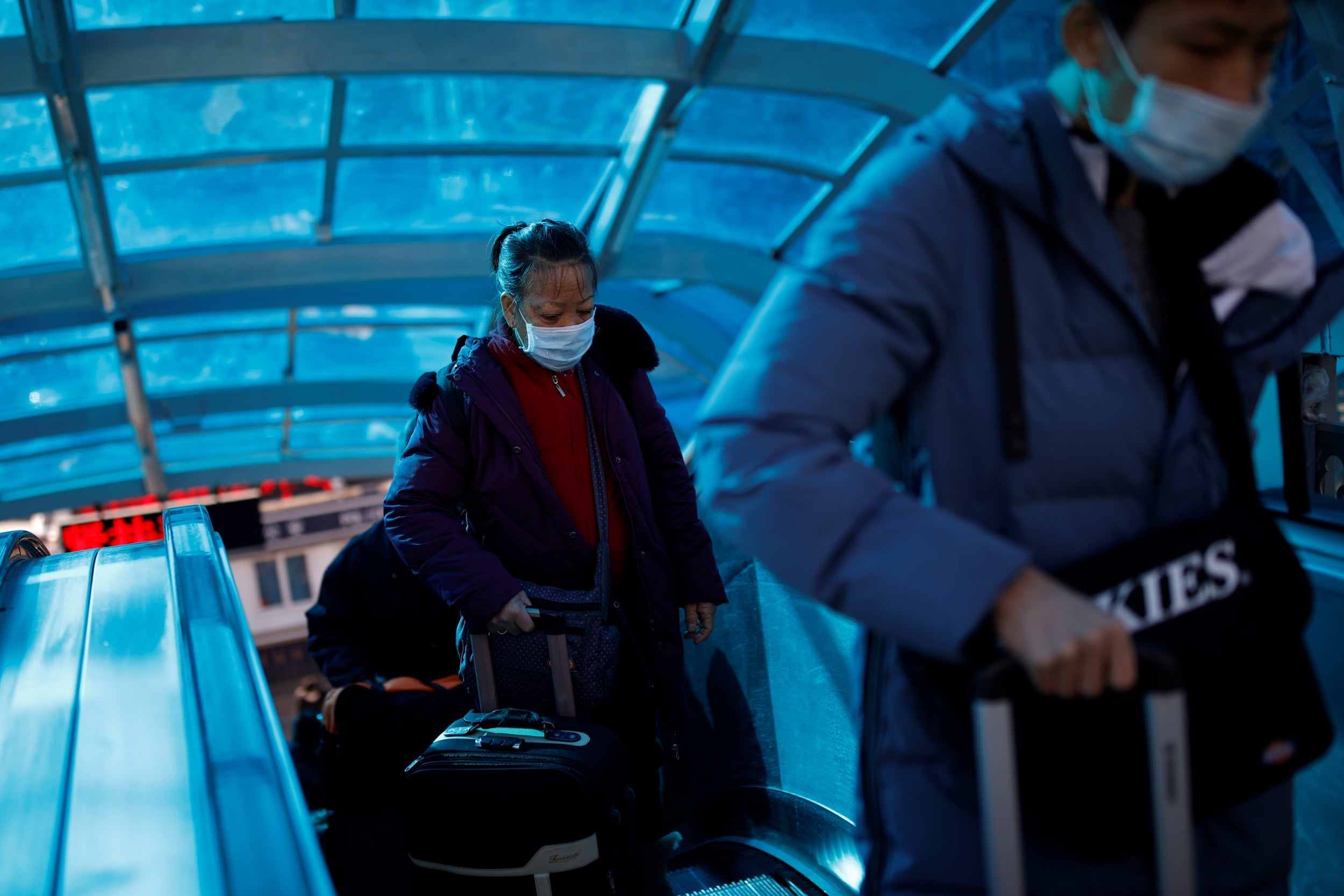People wear face masks on an escalator near Beijing Railway Station