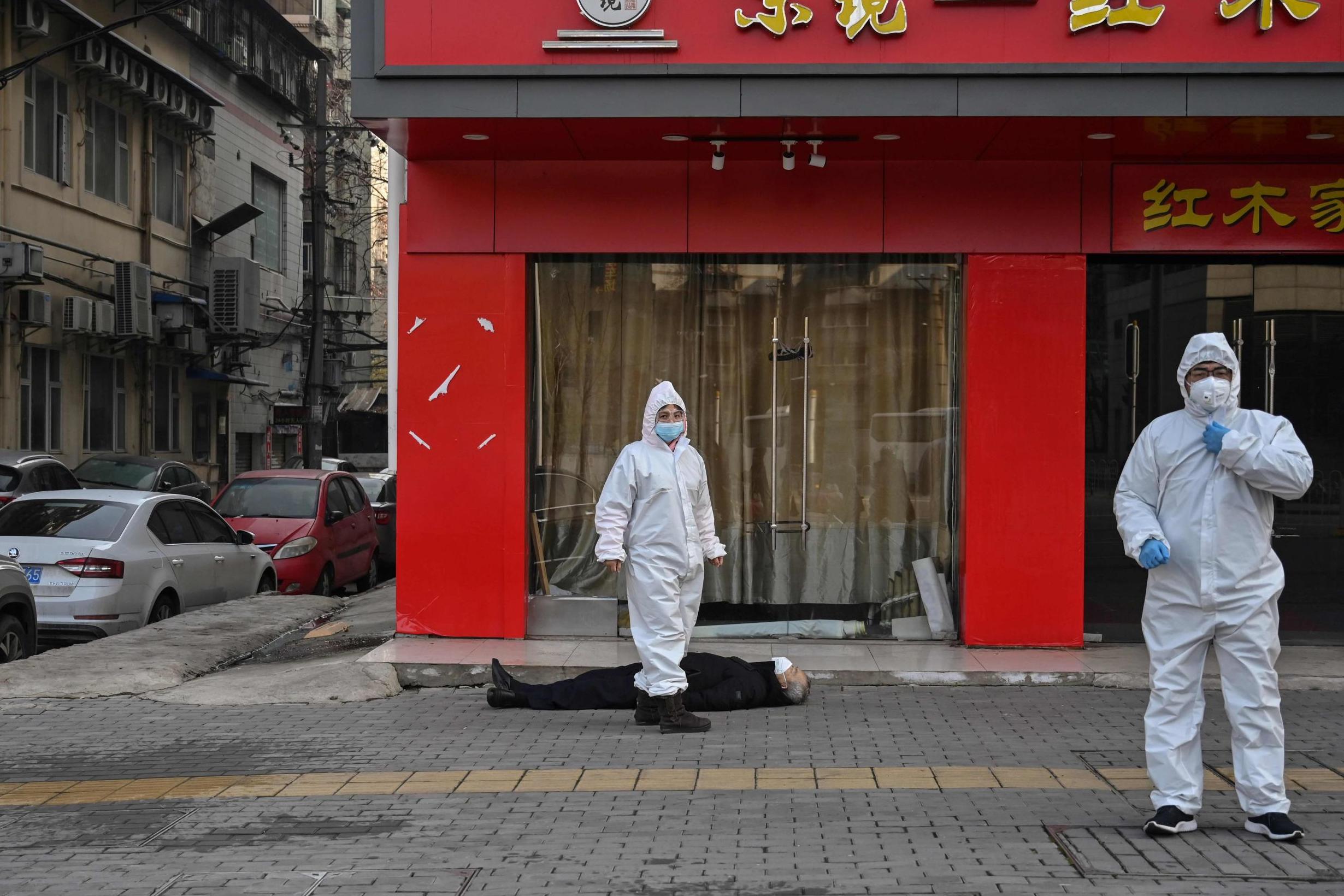 Officials attend the body of an elderly man who collapsed and died on a street near a hospital in Wuhan last week (AFP/Getty)