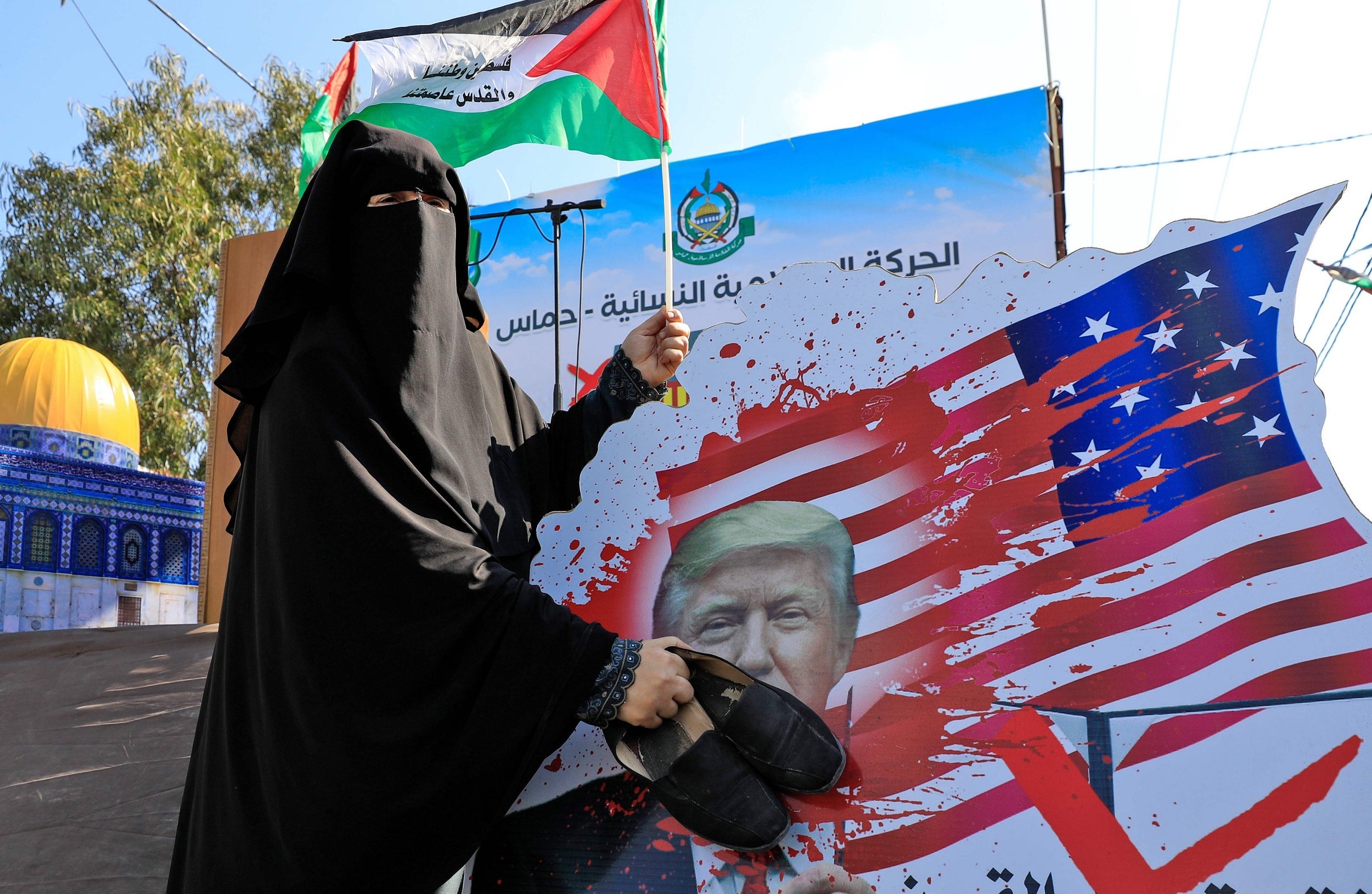 A Palestinian woman slams her shoes on a portrait of Trump during a demonstration in Gaza City