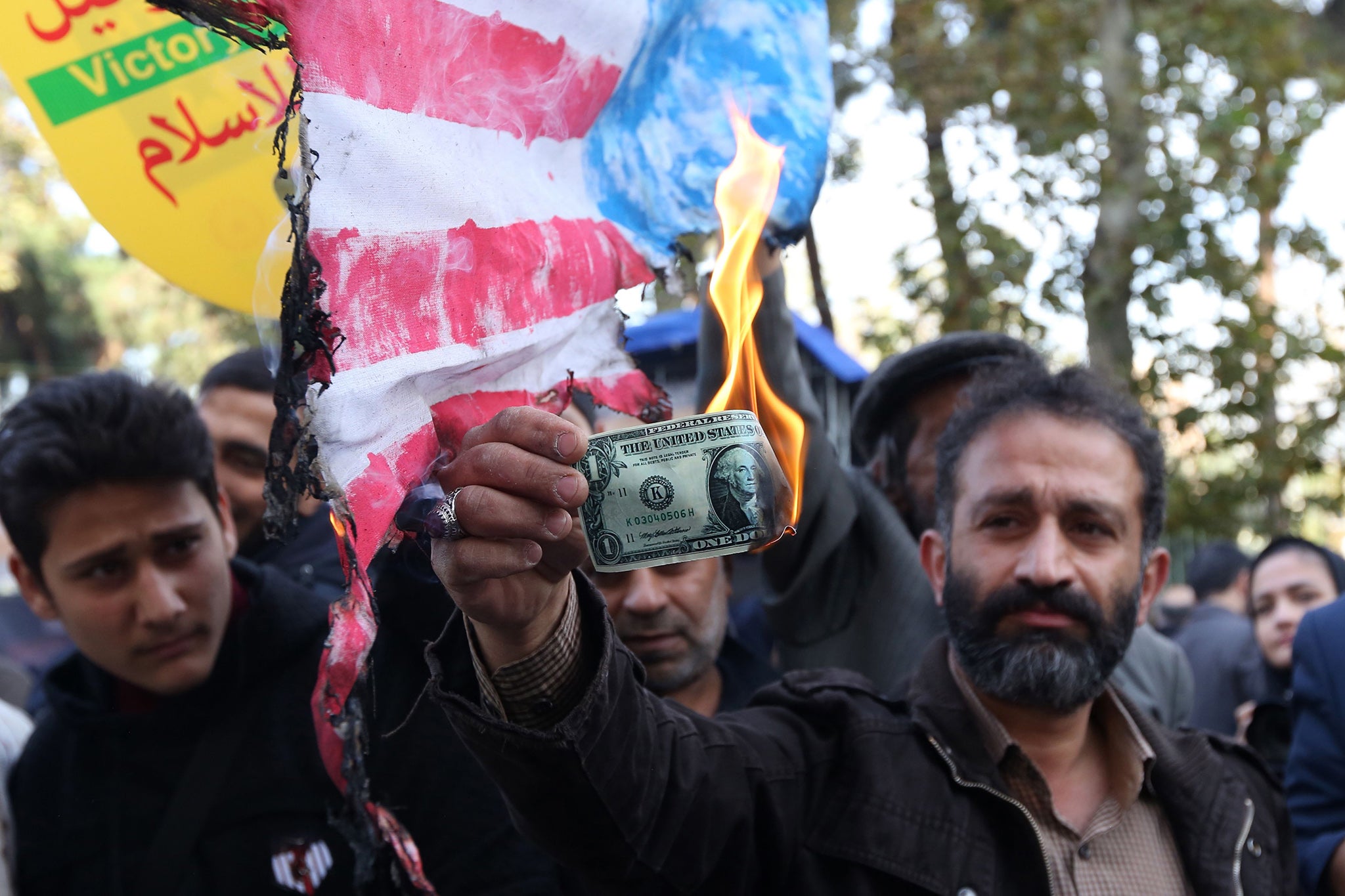 On the eve of renewed sanctions by Washington in 2018, an Iranian protester burns a dollar banknote in Tehran