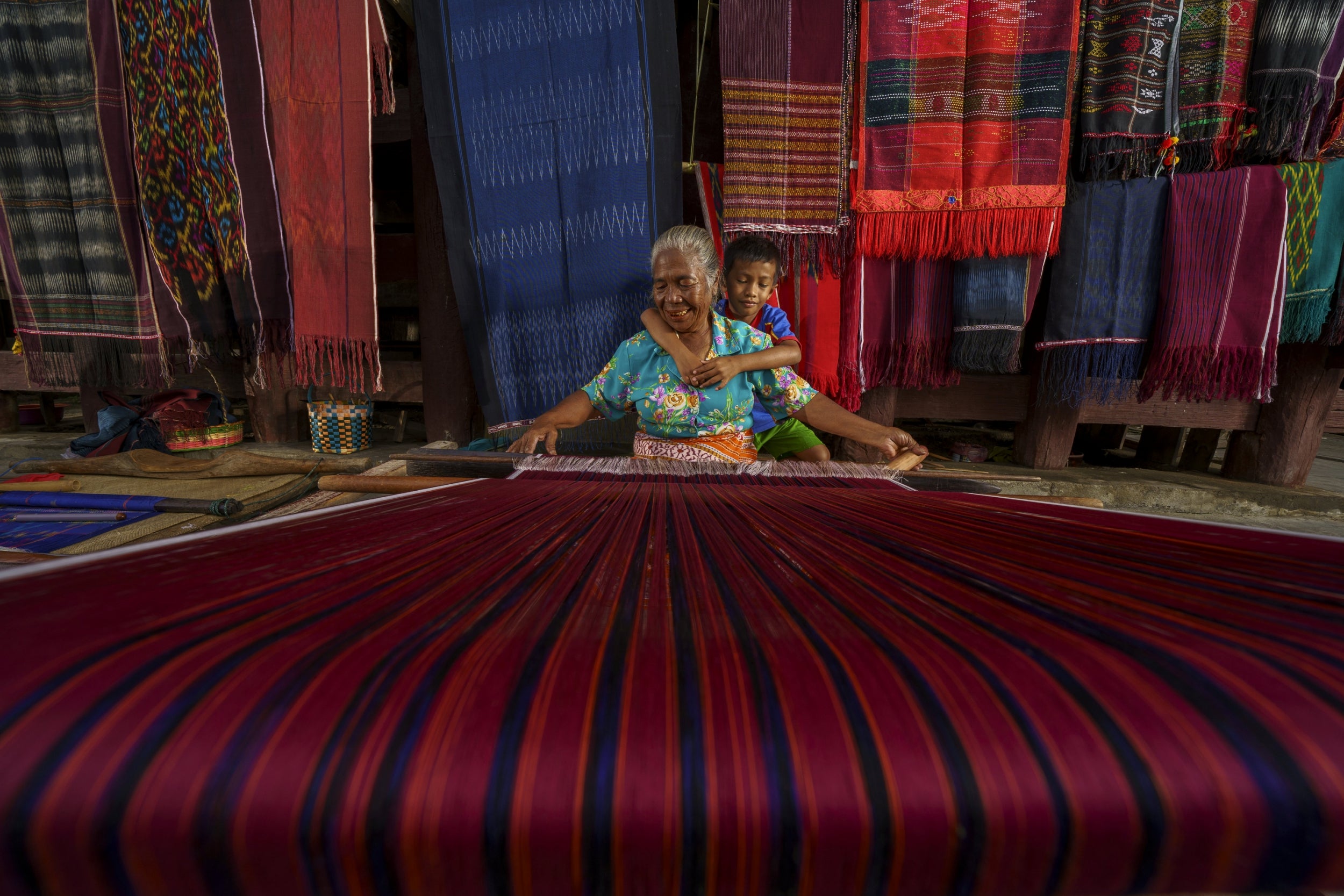 'I visited the area which is quite famous for its Ulos handwoven textile fabrics. The craftswoman's grandson hugged her from behind, and she welcomed him with a happy smile.' 

Location: Samosir Island, North Sumatera, Indonesia.