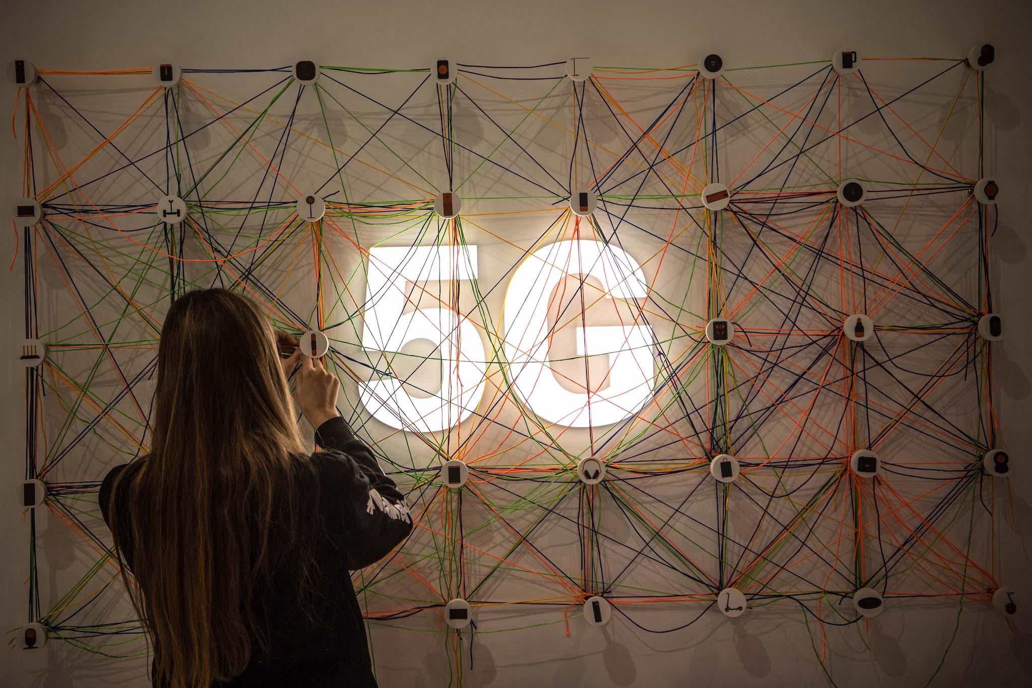 A staff member works next to a 5G logo at the Xiaomi booth on day 2 of the GSMA Mobile World Congress 2019 on February 26, 2019 in Barcelona, Spain