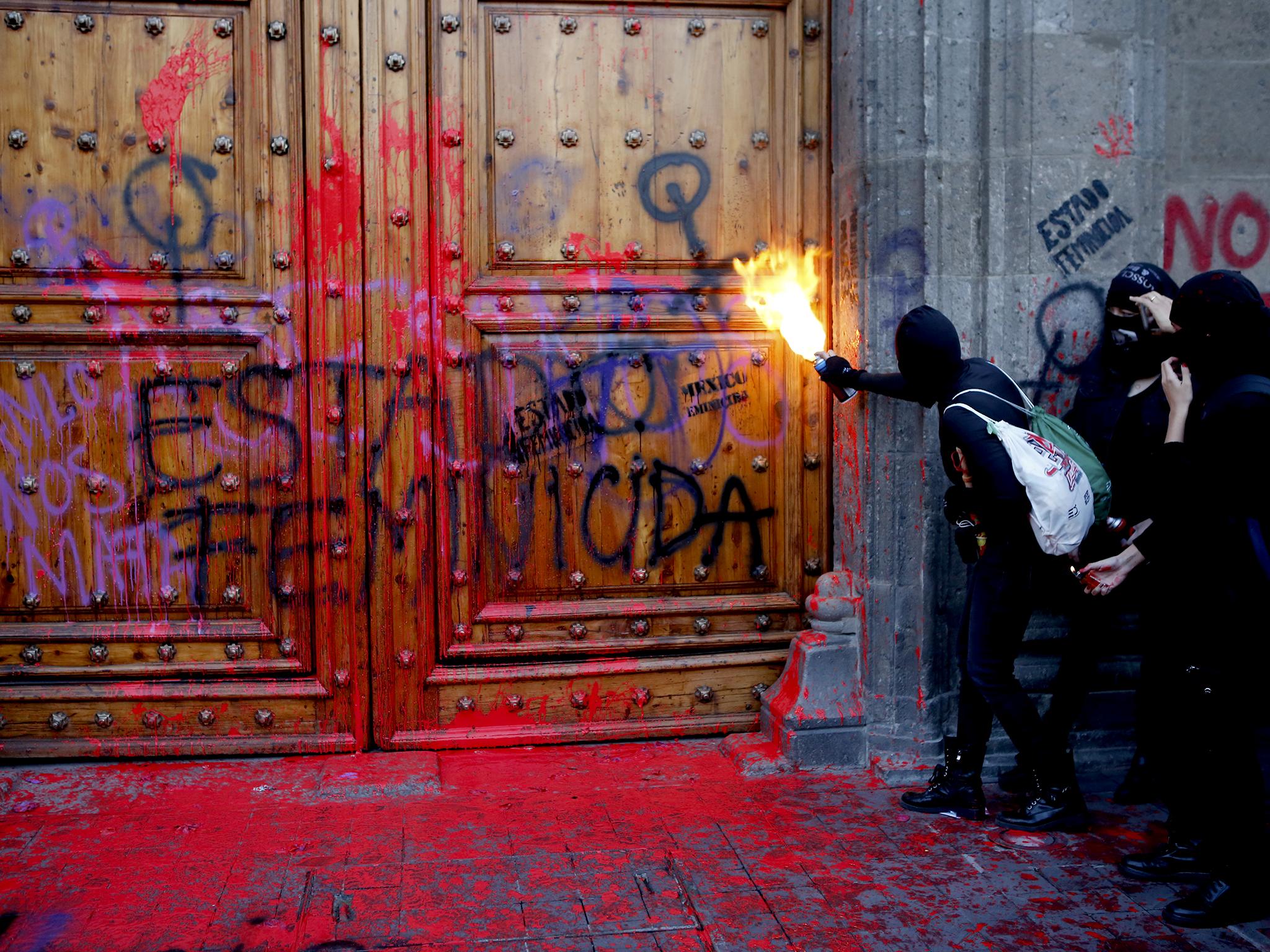 'Femicide state' is graffitied on the Mexican president's residence as a protester sprays fire at the door