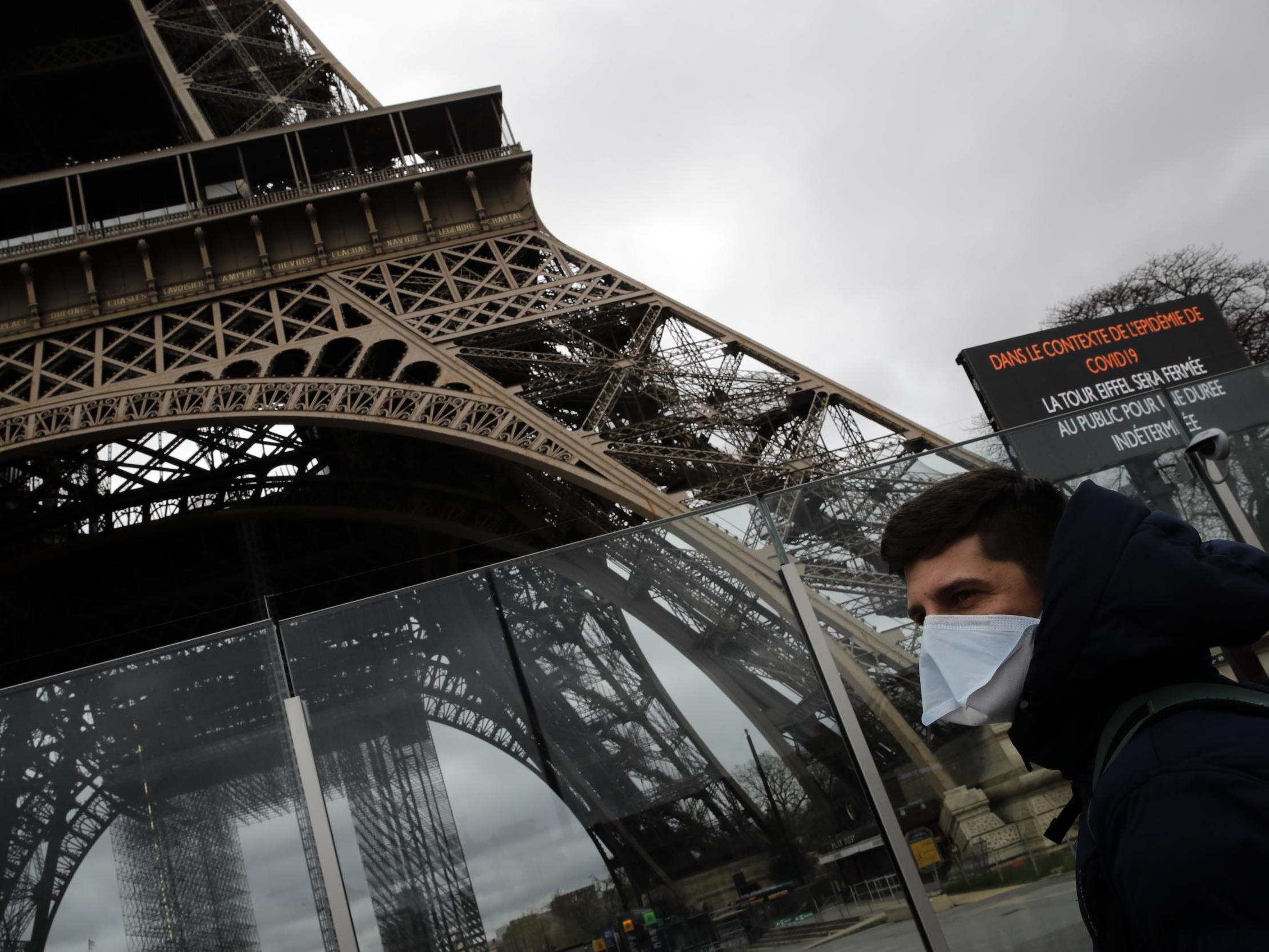 A man in a mask walks pasts the Eiffel tower, which is closed because of a ban on gatherings of more than 100 people