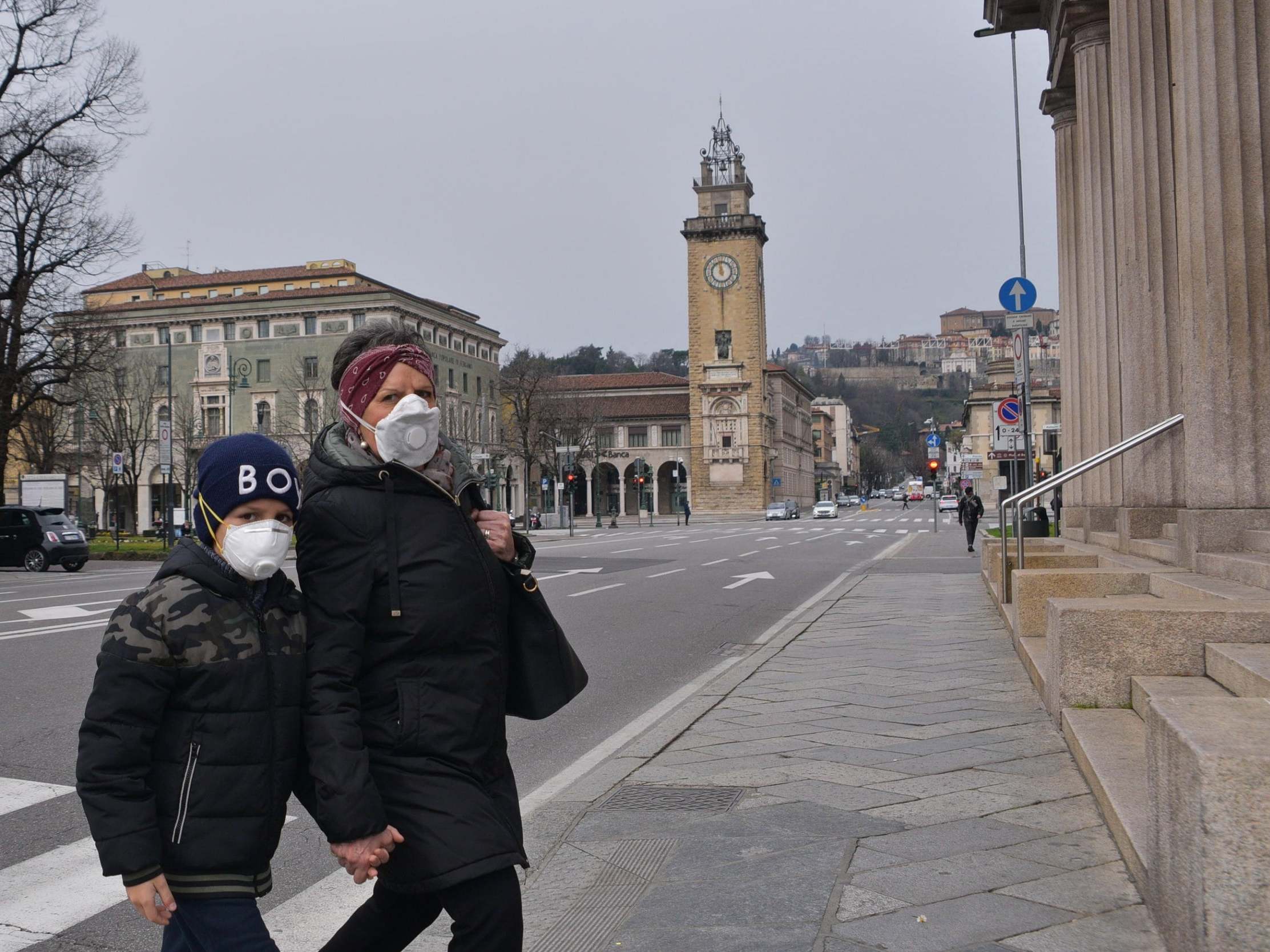 A woman and a child wearing face masks cross a road in the nearly-deserted city of Bergamo (EPA)