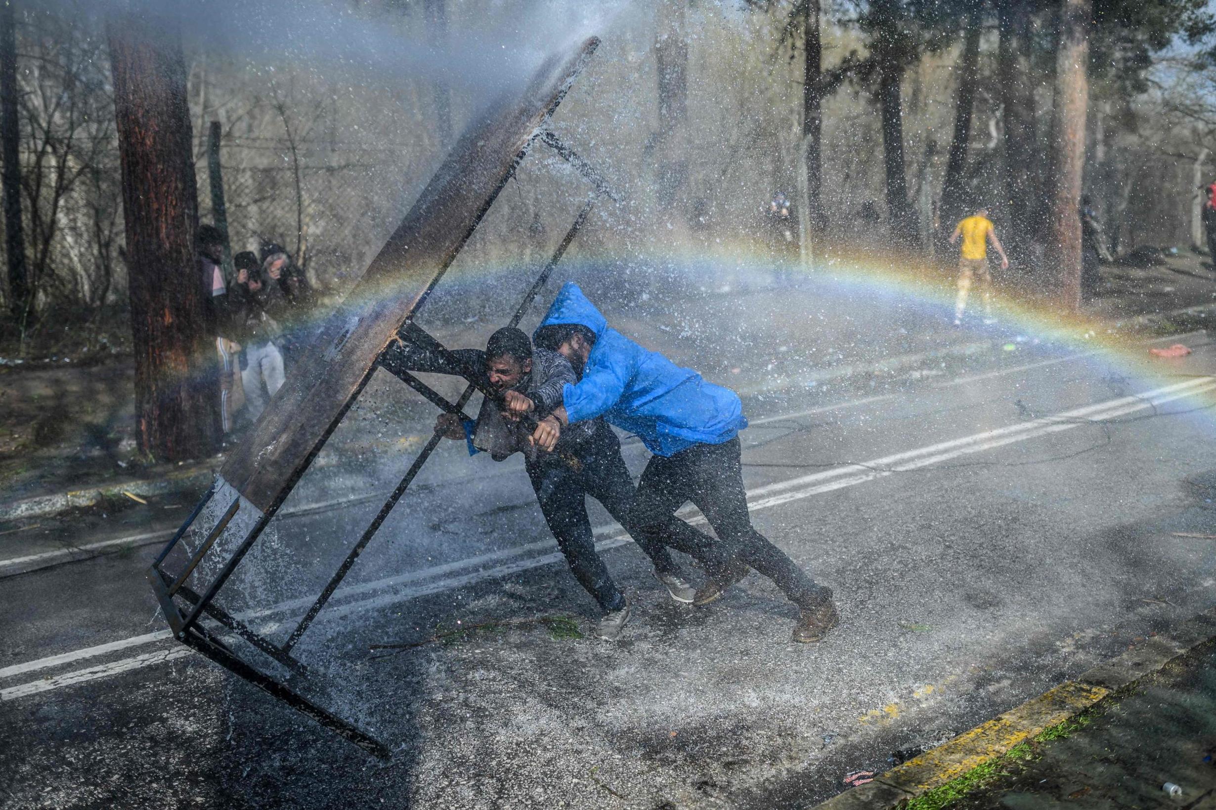 Migrants take cover behind a wooden board as Greek police use water cannons to block them from breaking fences at the Turkish-Greek border (AFP/Getty)