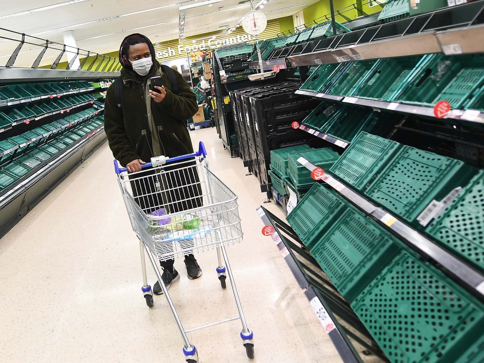 A shopper passes empty shelves at a Tesco supermarket in London