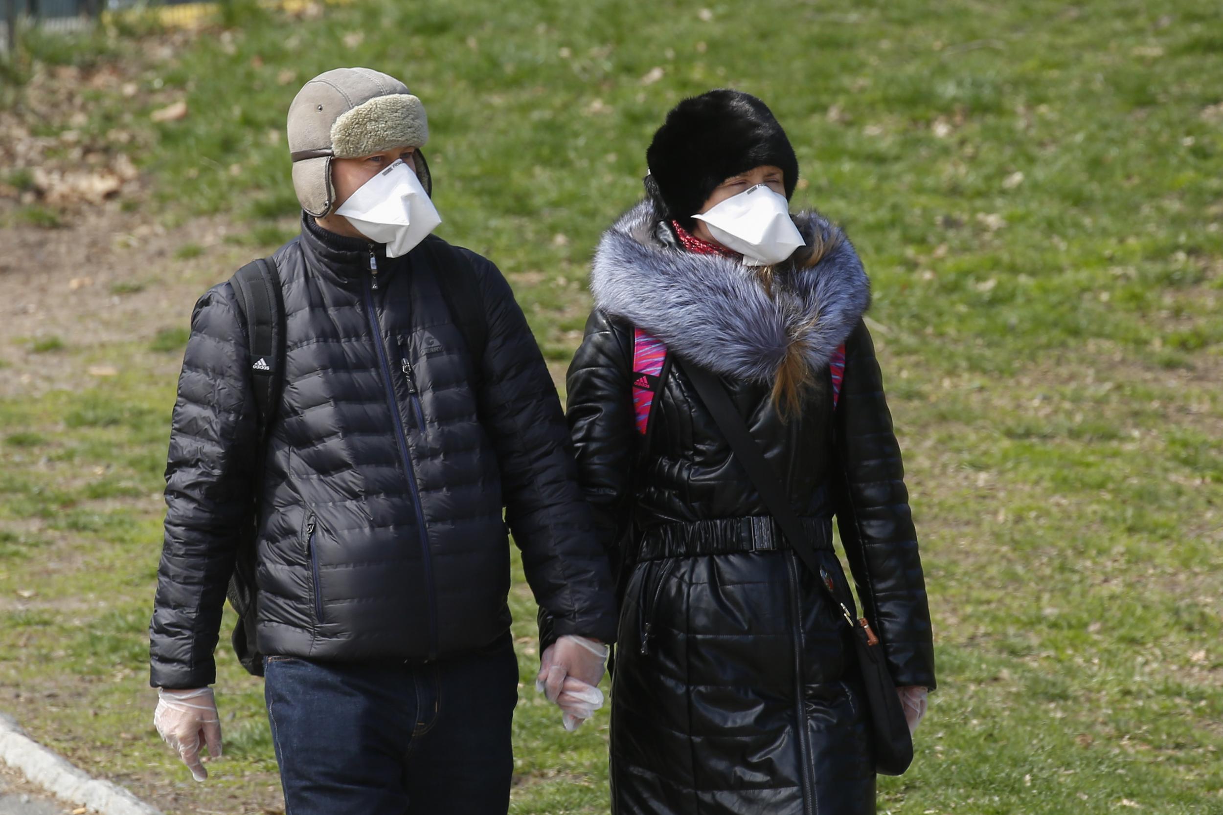 A couple wears face masks and surgical gloves as they walk in NYC’s Central Park