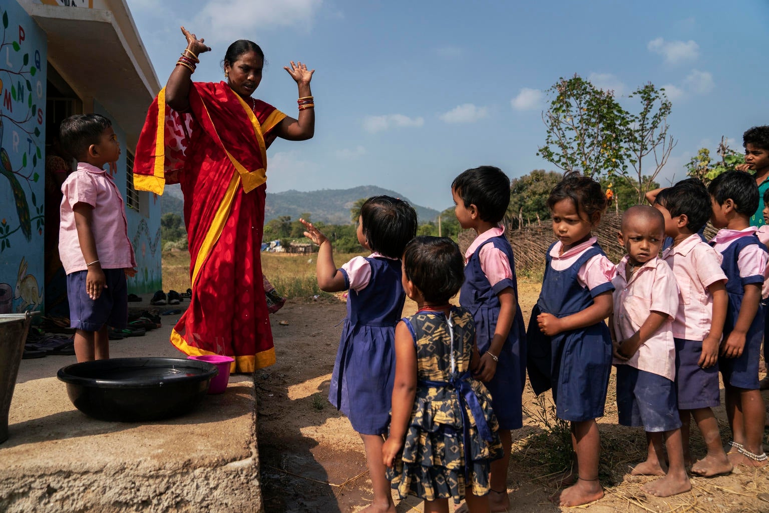 Children in India are taken outside to wash their hands before they receive their mid-day meal. A healthcare worker ensures they are washing their hands correctly