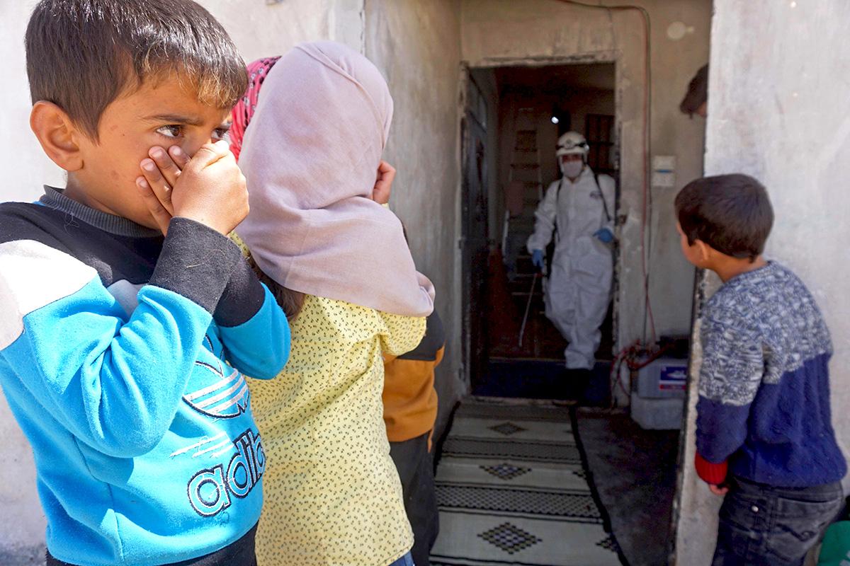Virus fight: Syrian children look on as the White Helmets disinfect a former school building in Binnish
