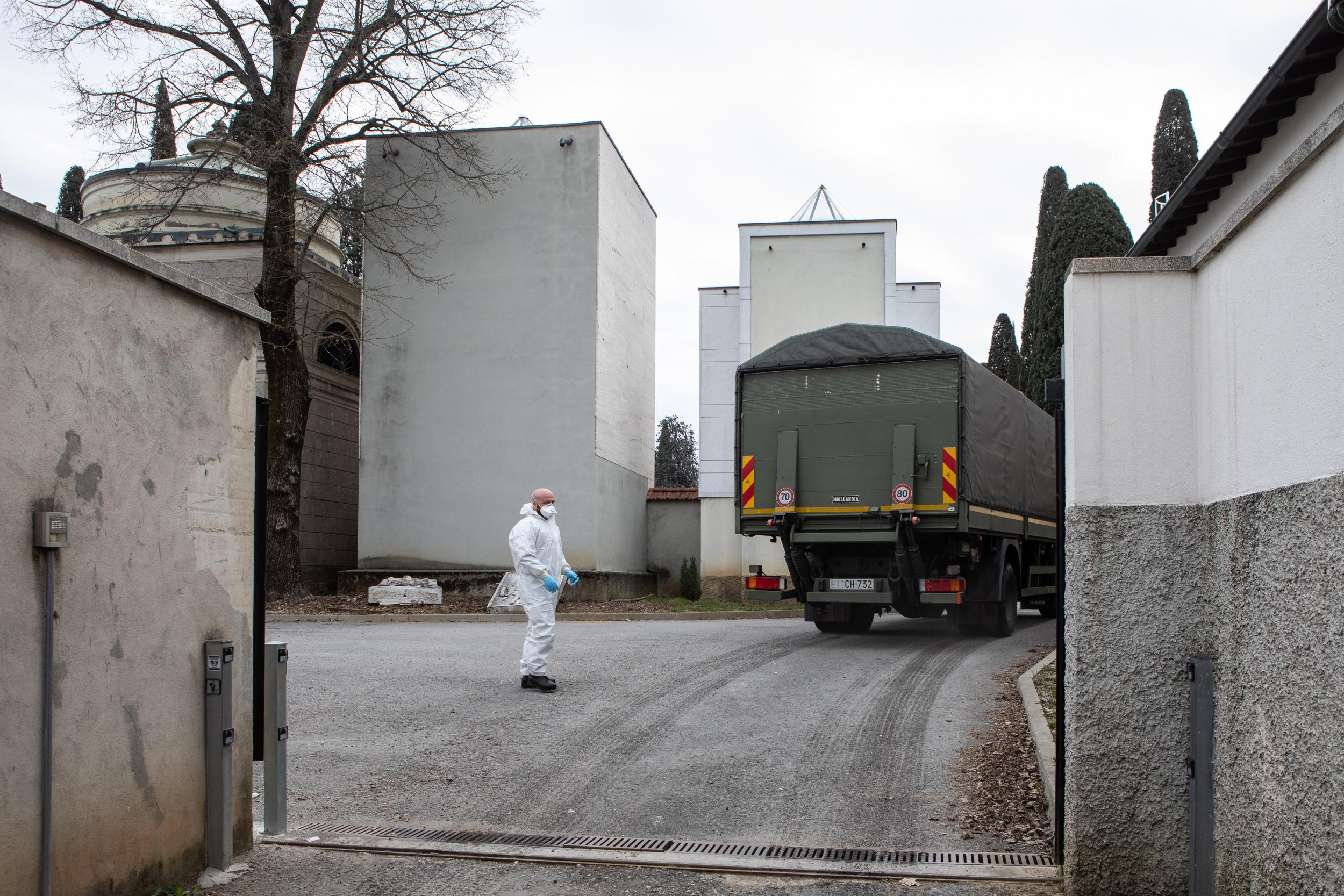 An Italian army officer wearing a protective suit stands as a military vehicle drives in the Monumental Cemetery on March 26 in Bergamo