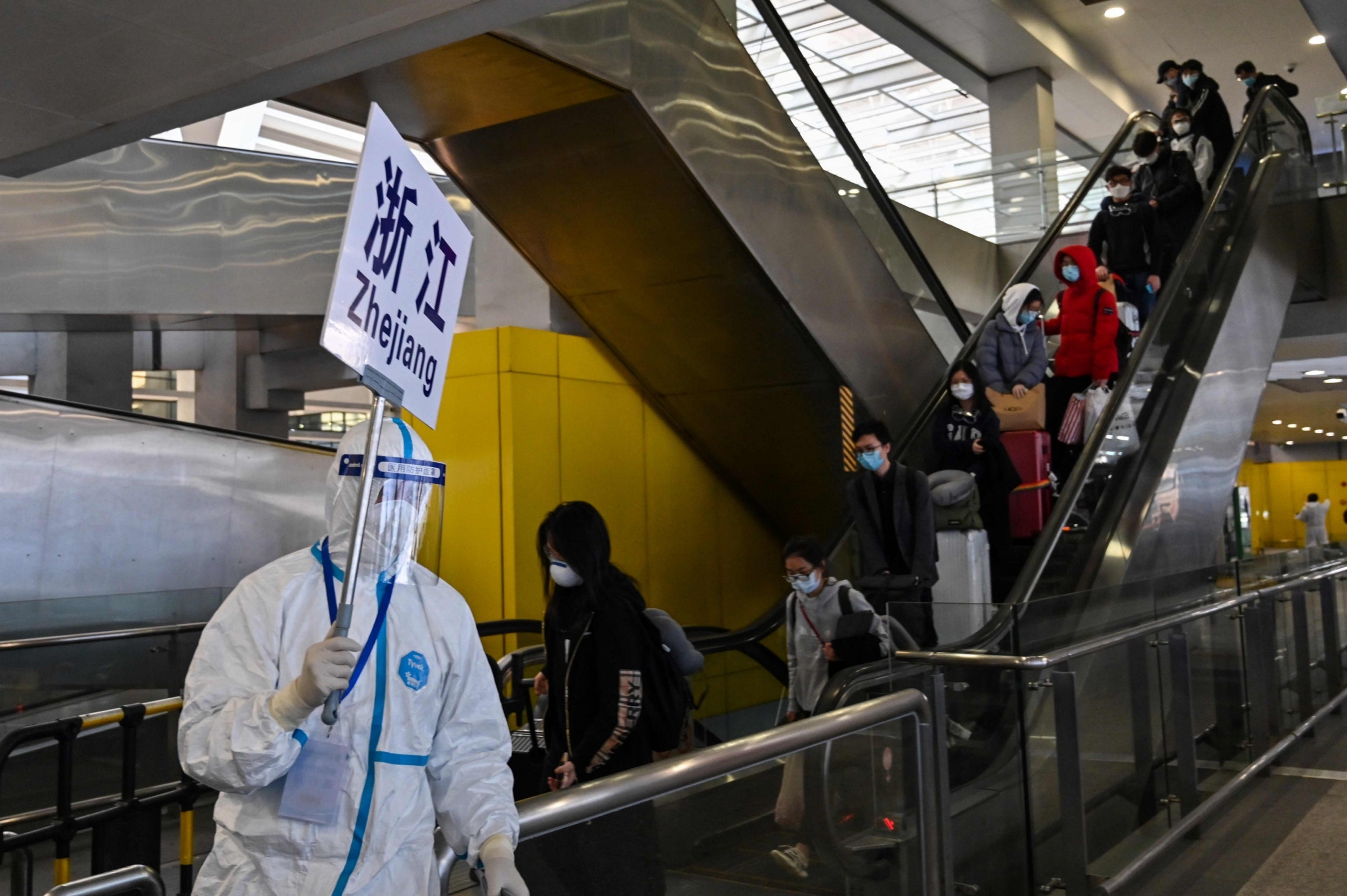 A worker wearing protective gear escorts passengers after they arrived in Shanghai to a bus that will take them to Zhejiang province