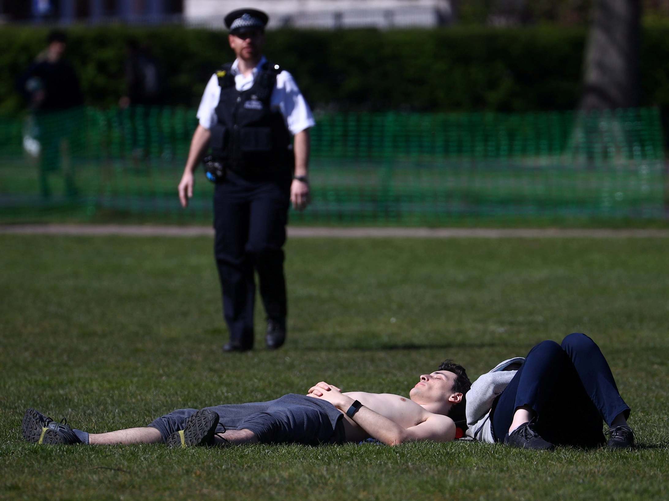 A police officer approaches a sunbather in Greenwich Park, south London.
